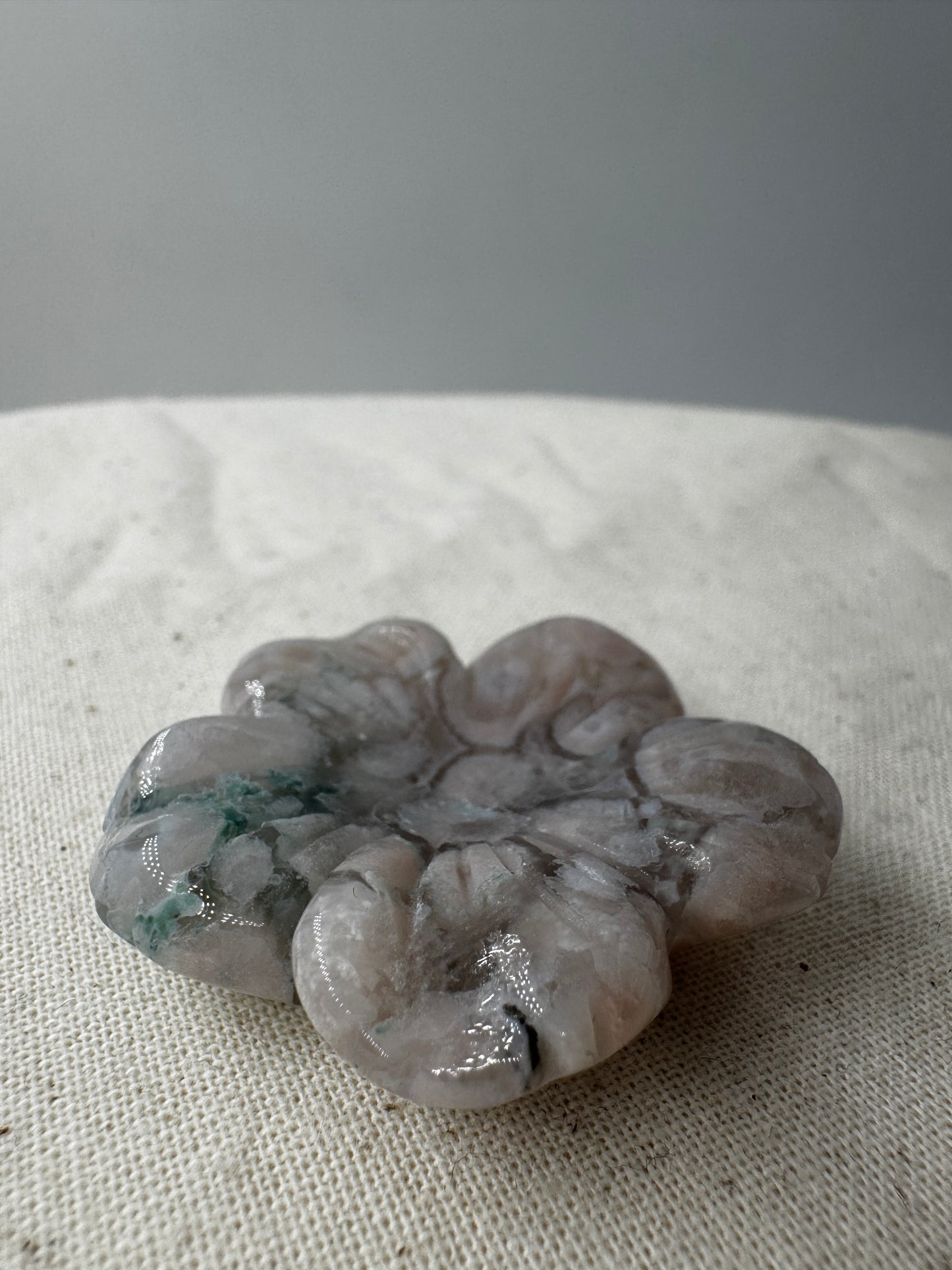 Eine detailreiche Skulptur in Blumenform aus zartrosa Blumenachat mit deutlich erkennbaren, weißen sphärolithischen Einschlüssen.