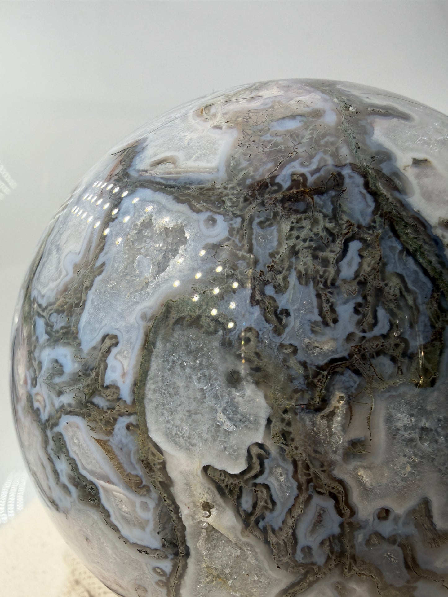 Eine hochglanzpolierte Moosachat-Kugel mit tiefgrünen, pflanzenähnlichen Strukturen in einer teils transparenten Matrix.