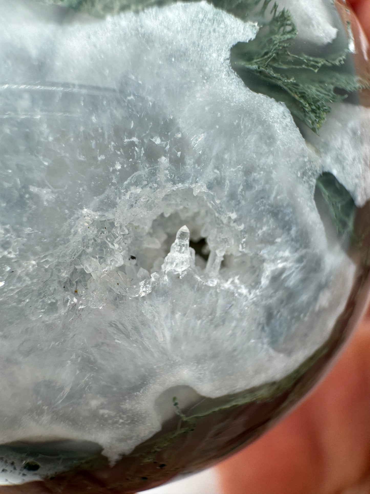 Eine hochglanzpolierte Moosachat-Kugel mit tiefgrünen, pflanzenähnlichen Strukturen in einer teils transparenten Matrix.