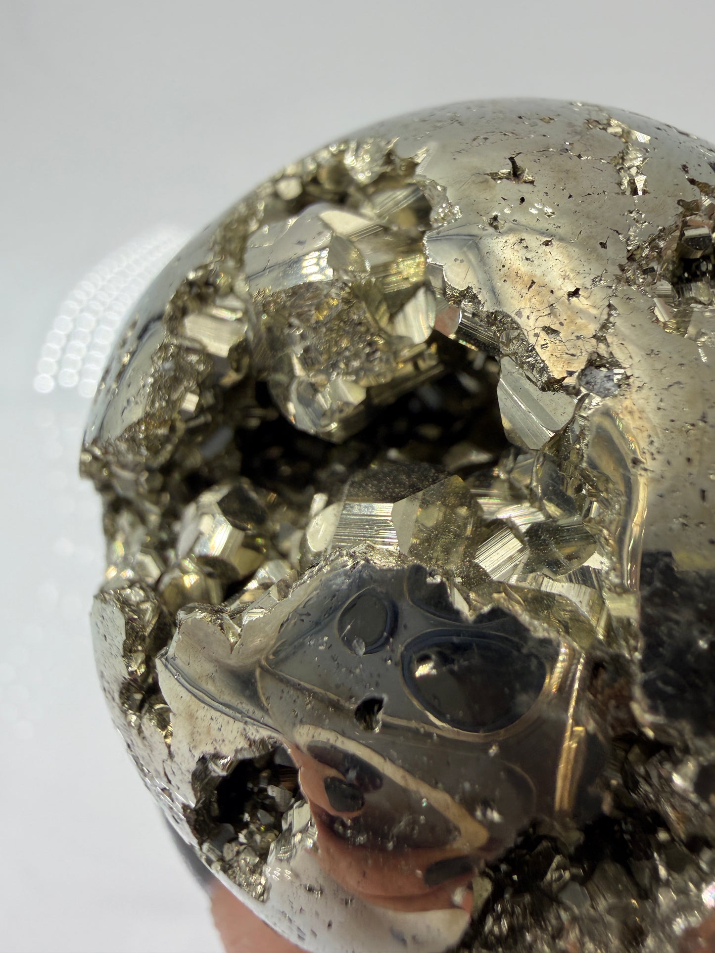 Eine hochglänzende, metallisch Pyrit-Kugel, deren spiegelnde Oberfläche die Umgebung reflektiert und winzige, natürliche Kristallstrukturen offenbart.