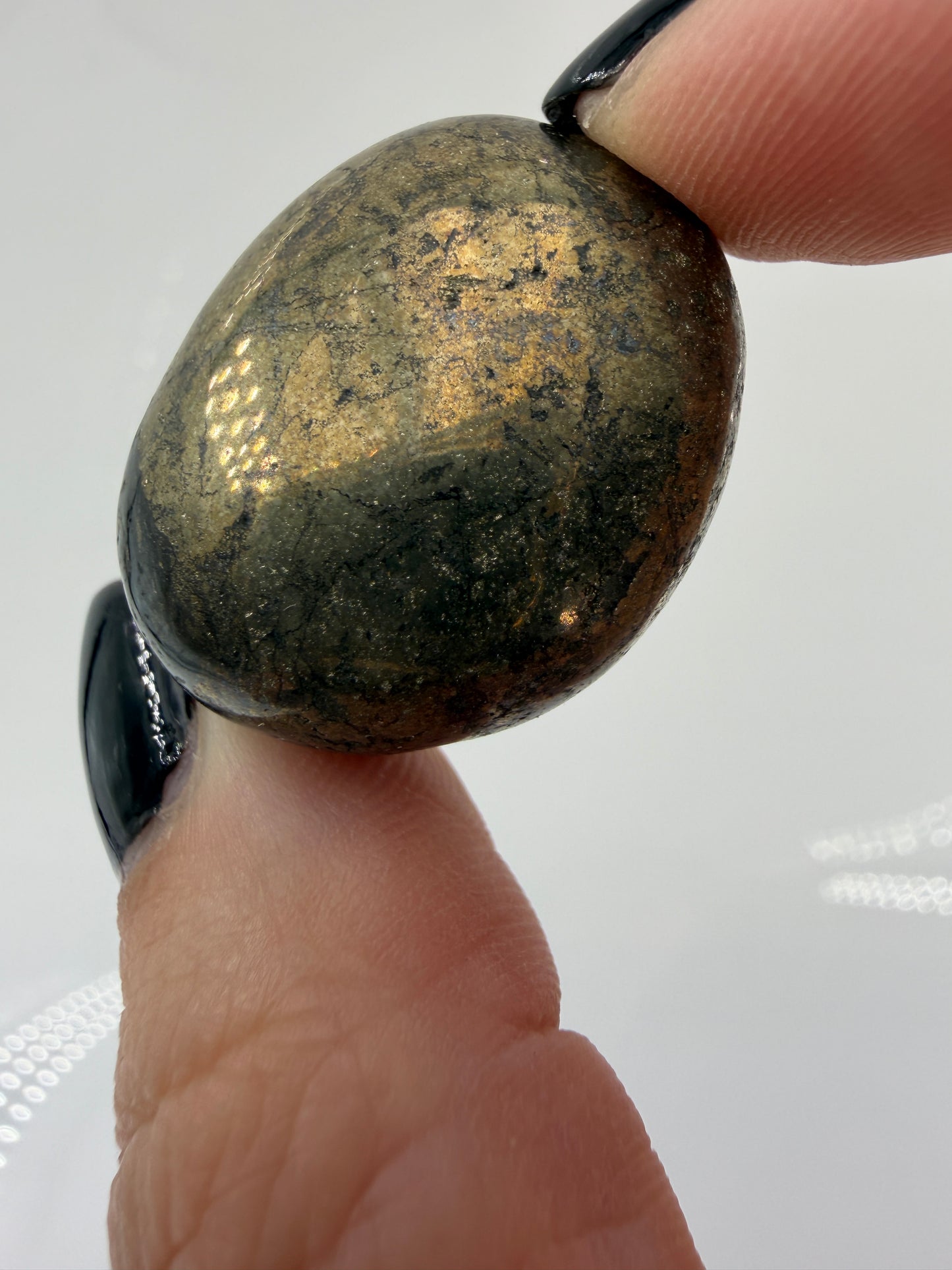 Ein glänzender Pyrit-Trommelsteinen, der durch sein hohes Gewicht und ihre spiegelnden, metallischen Oberflächen beeindruckt.