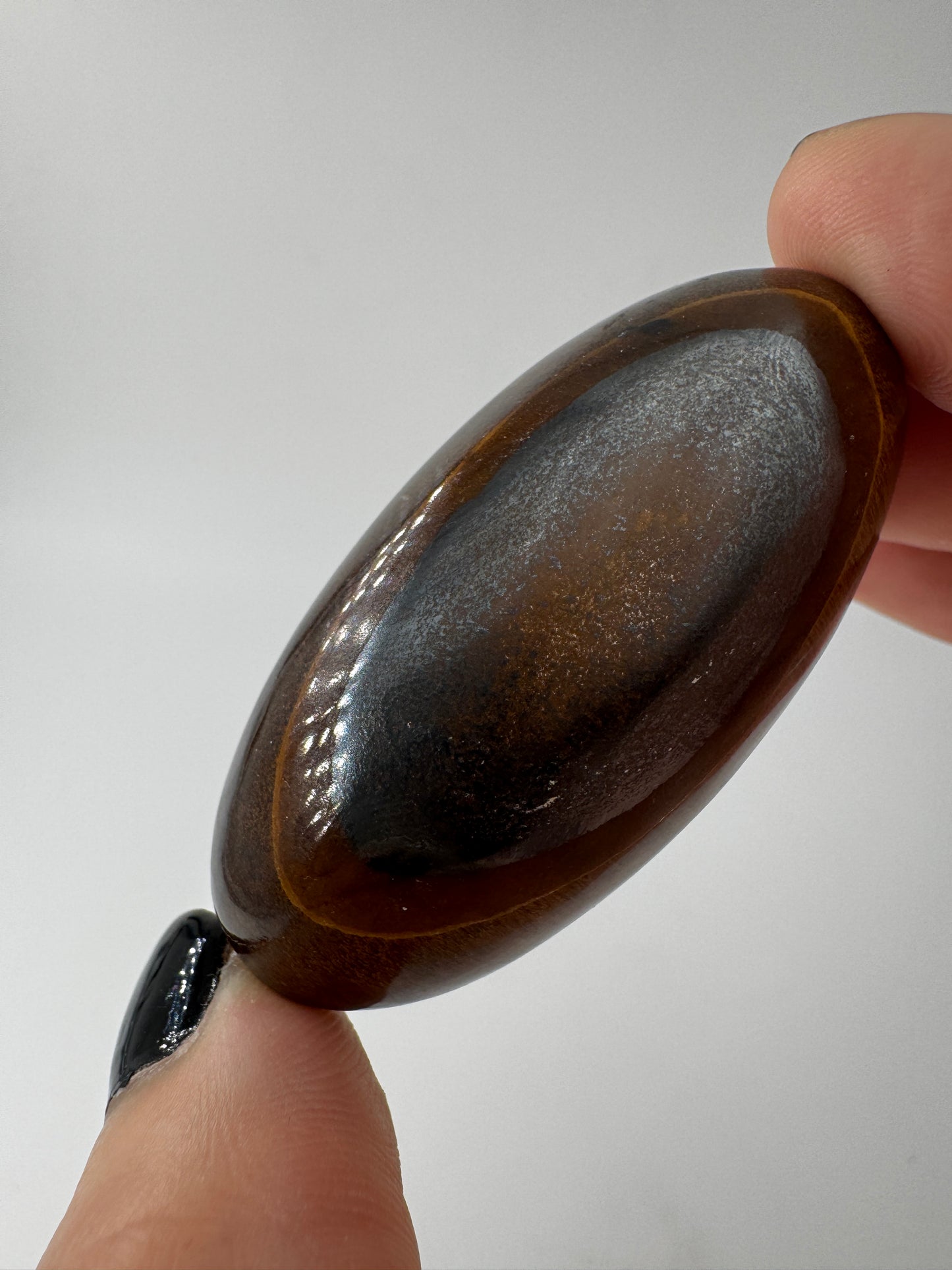 Ein eiförmig poliertes Tigerauge mit lebhaftem, goldbraunem Schimmer und einer perfekt glatten, reflektierenden Oberfläche.
