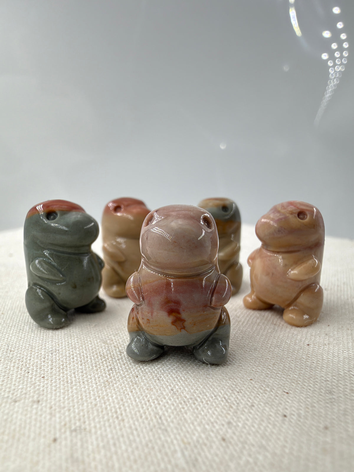polierte Dinosaurierfiguren aus Alashan Achat in Rosa-, Beige- und Graugrüntönen auf hellem Untergrund.