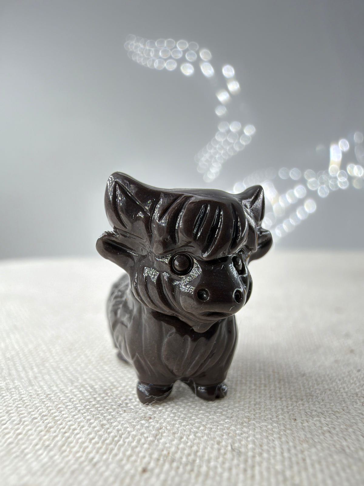 Kuhfigur aus Alashan Achat in schwarz mit zotteliger Fellstruktur und kleinen Hörnern auf hellem Untergrund