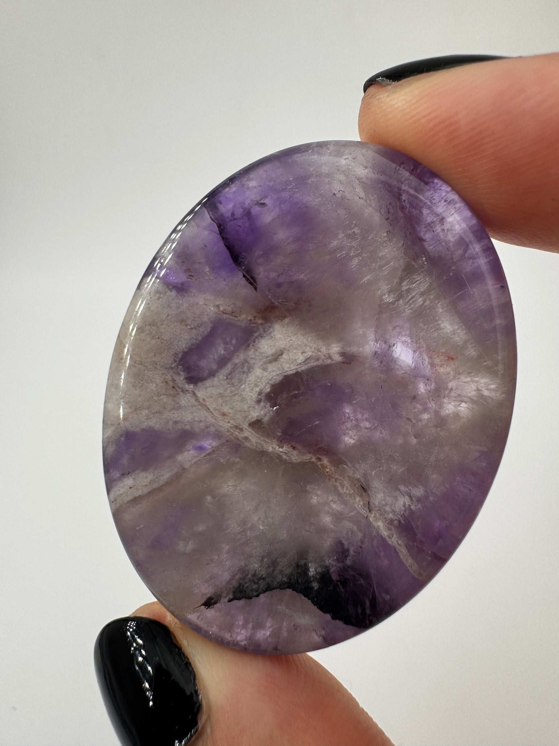 Ein  Daumensteinen aus Amethyst mit glänzend polierten Oberflächen und zentraler Daumenmulde.