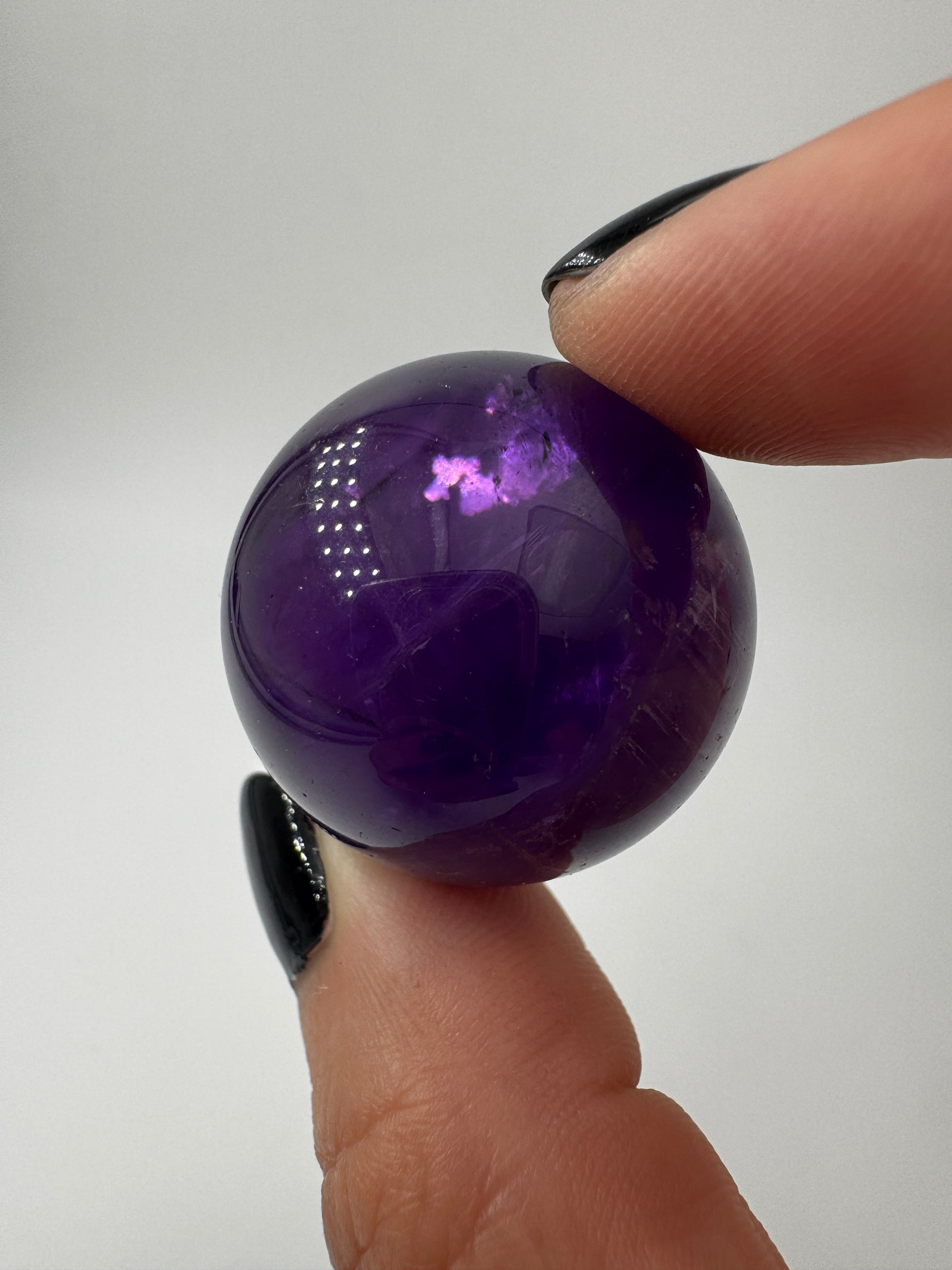 Eine hochglanzpolierte Amethyst-Kugel mit tiefvioletten Farbzentren und natürlichen Wachstumsstrukturen.