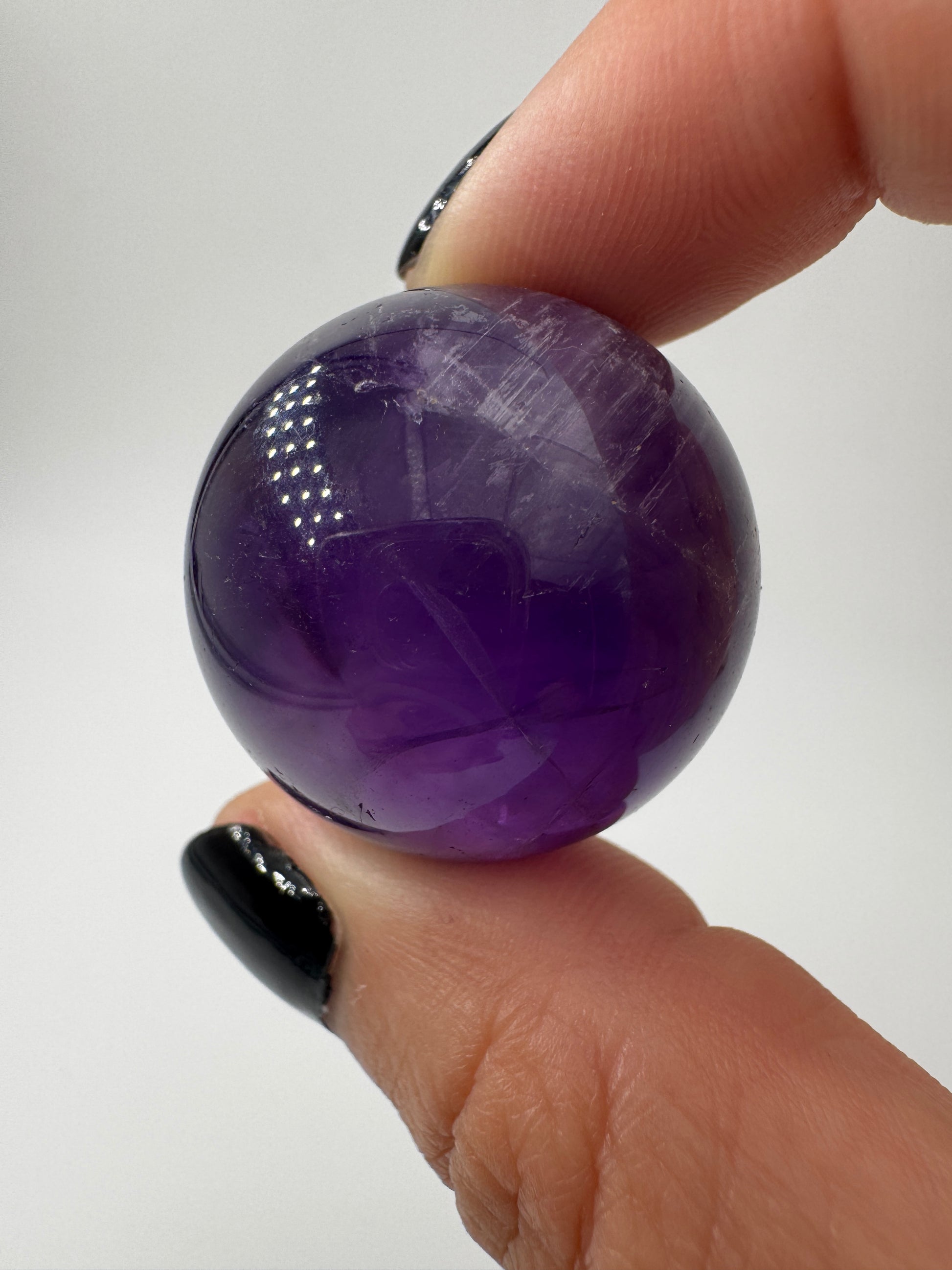 Eine hochglanzpolierte Amethyst-Kugel mit tiefvioletten Farbzentren und natürlichen Wachstumsstrukturen.