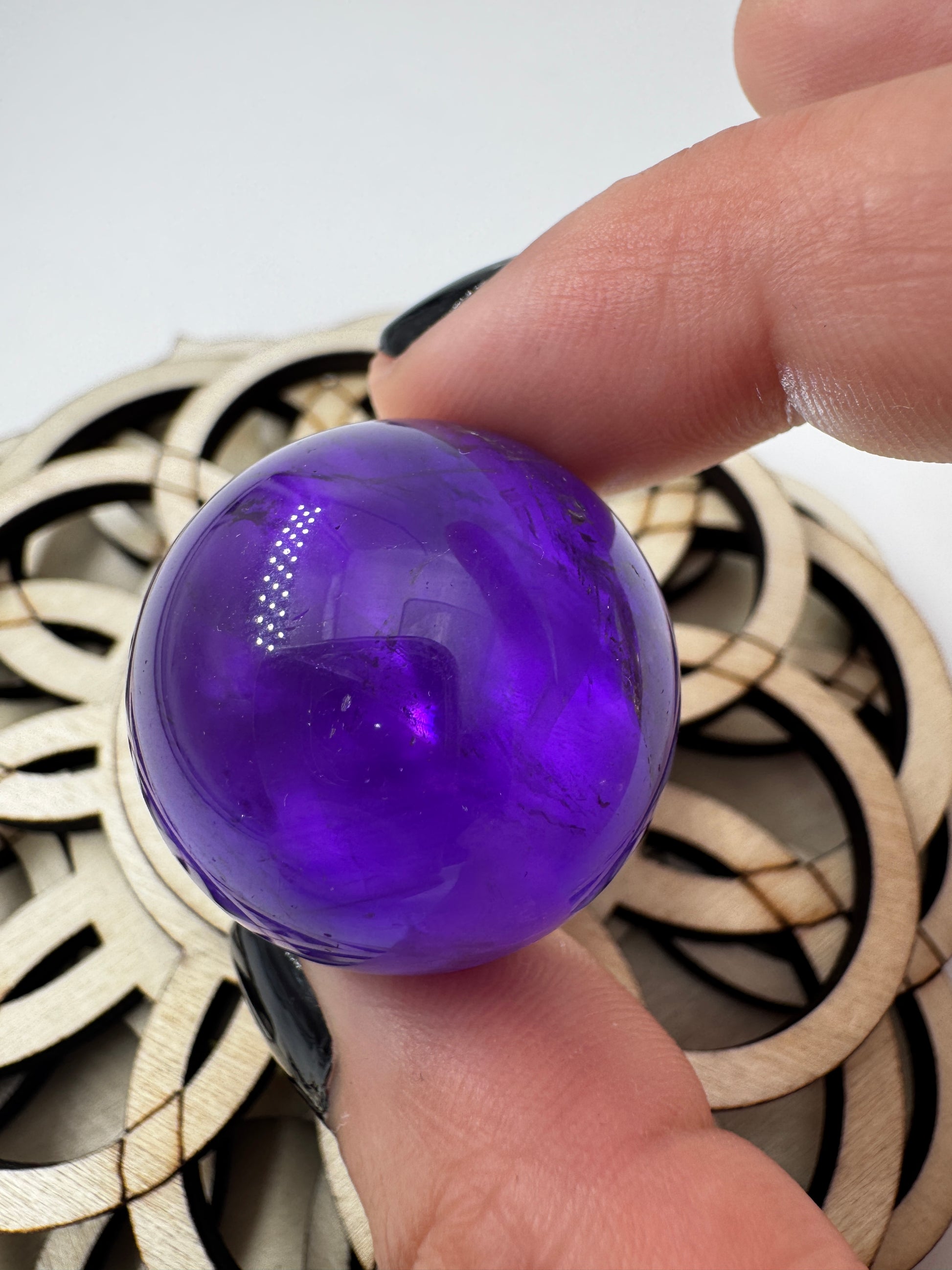 Eine hochglanzpolierte Amethyst-Kugel mit tiefvioletten Farbzentren und natürlichen Wachstumsstrukturen mit leichter Beleuchtung von hinten.