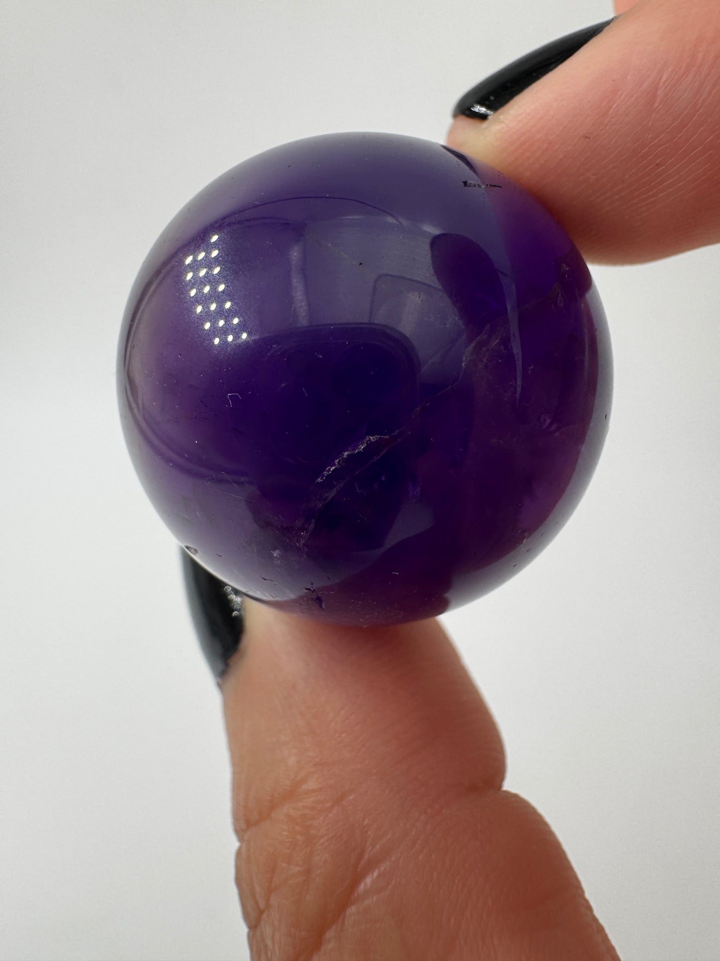 Eine hochglanzpolierte Amethyst-Kugel mit tiefvioletten Farbzentren und natürlichen Wachstumsstrukturen.
