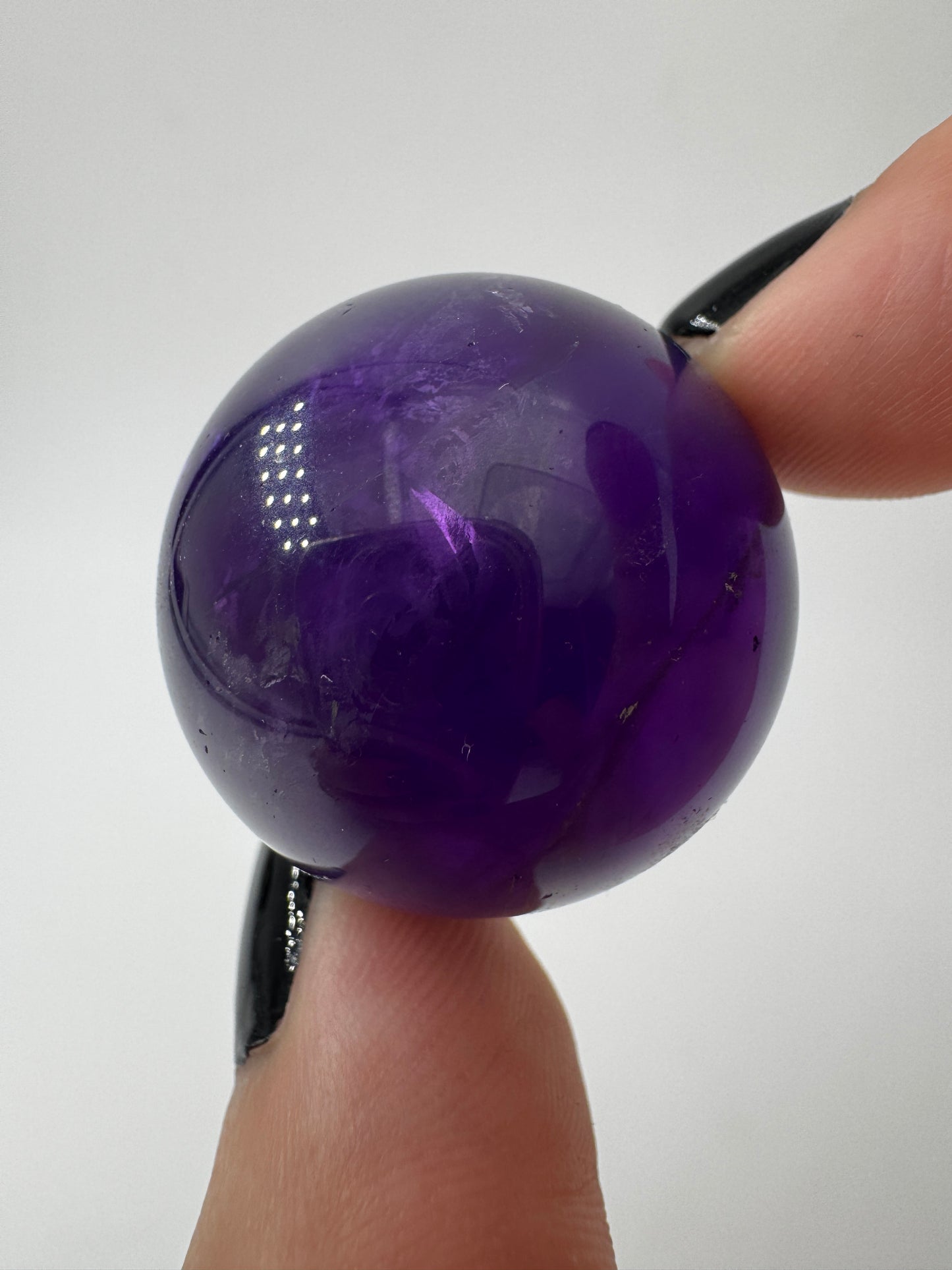 Eine hochglanzpolierte Amethyst-Kugel mit tiefvioletten Farbzentren und natürlichen Wachstumsstrukturen.
