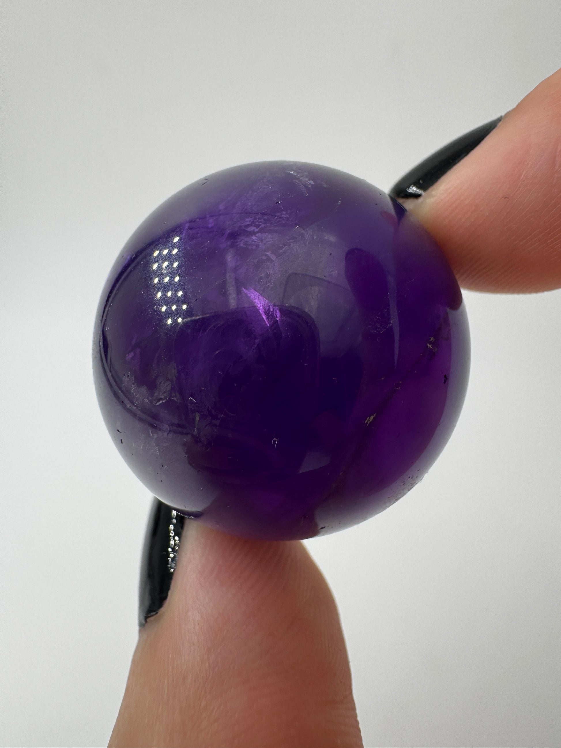 Eine hochglanzpolierte Amethyst-Kugel mit tiefvioletten Farbzentren und natürlichen Wachstumsstrukturen.