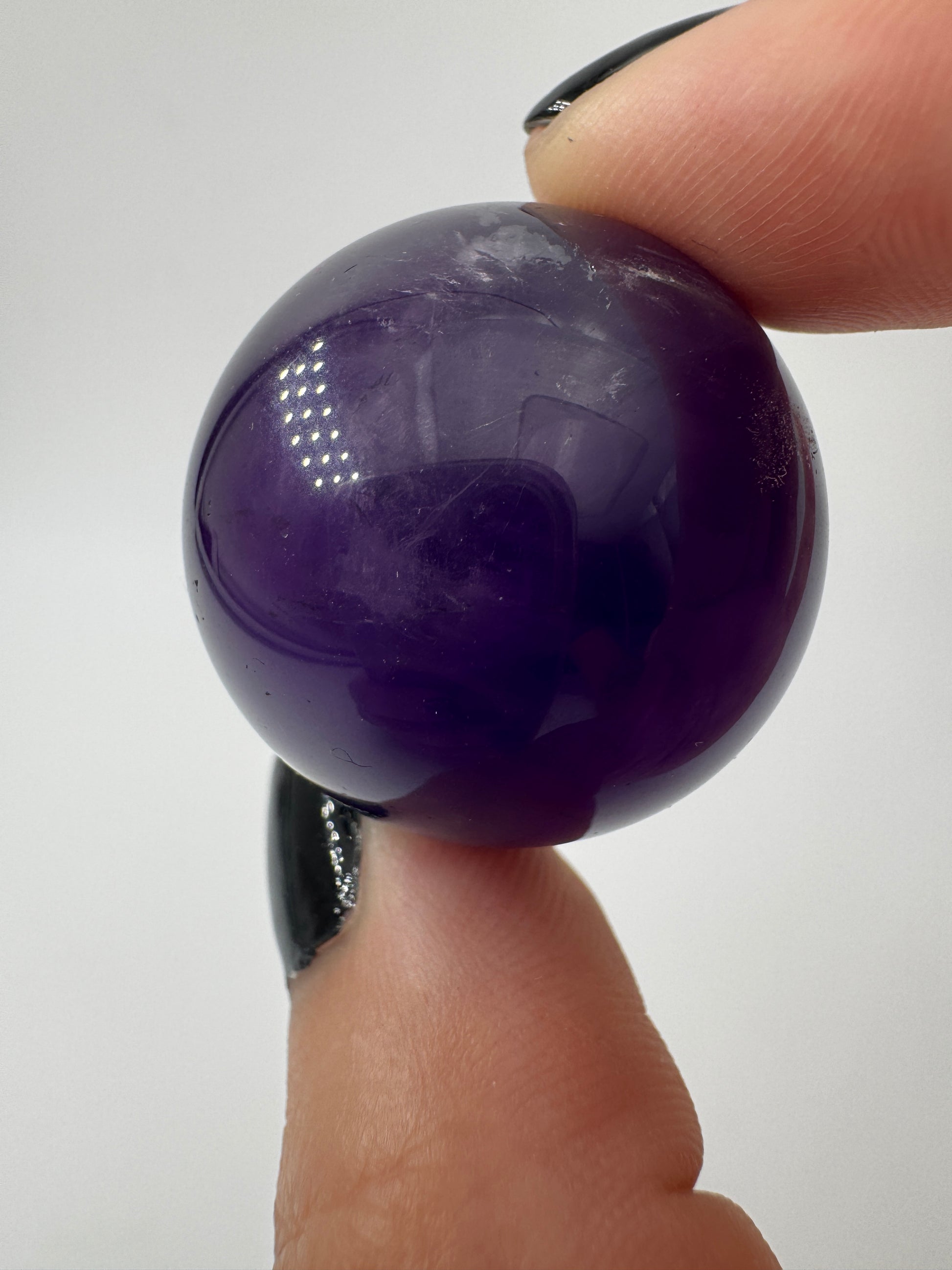 Eine hochglanzpolierte Amethyst-Kugel mit tiefvioletten Farbzentren und natürlichen Wachstumsstrukturen.