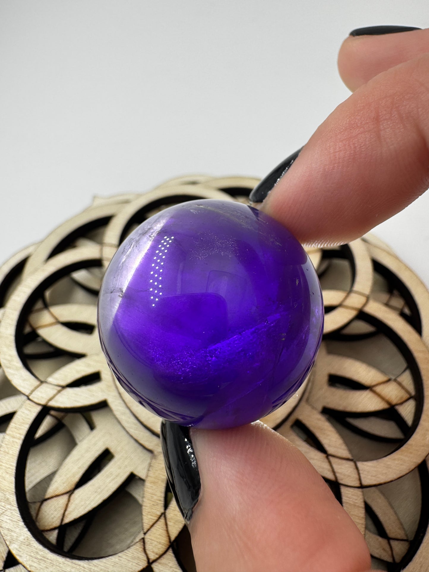 Eine hochglanzpolierte Amethyst-Kugel mit tiefvioletten Farbzentren und natürlichen Wachstumsstrukturen mit leichter Beleuchtung von hinten.