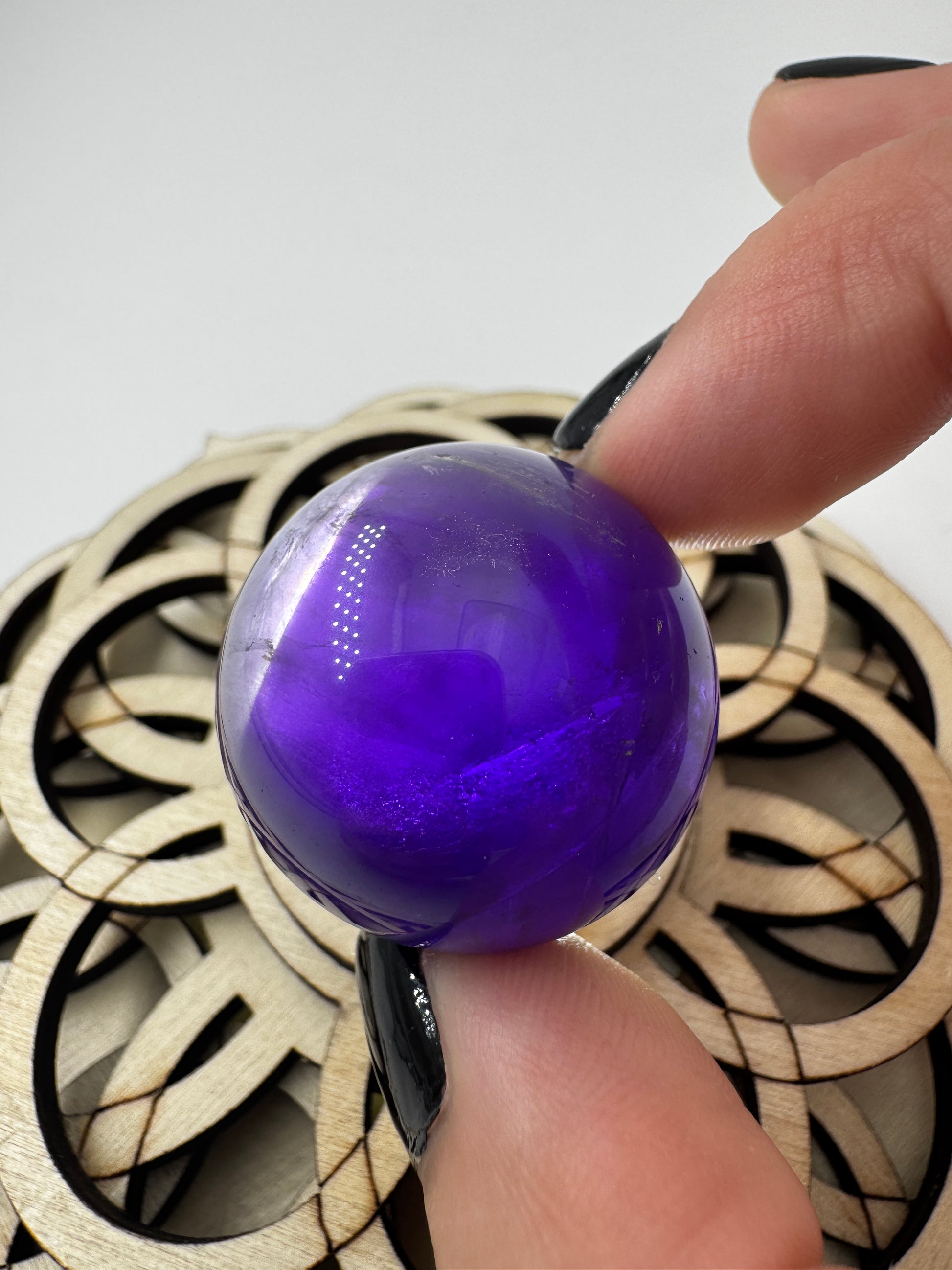 Eine hochglanzpolierte Amethyst-Kugel mit tiefvioletten Farbzentren und natürlichen Wachstumsstrukturen mit leichter Beleuchtung von hinten.