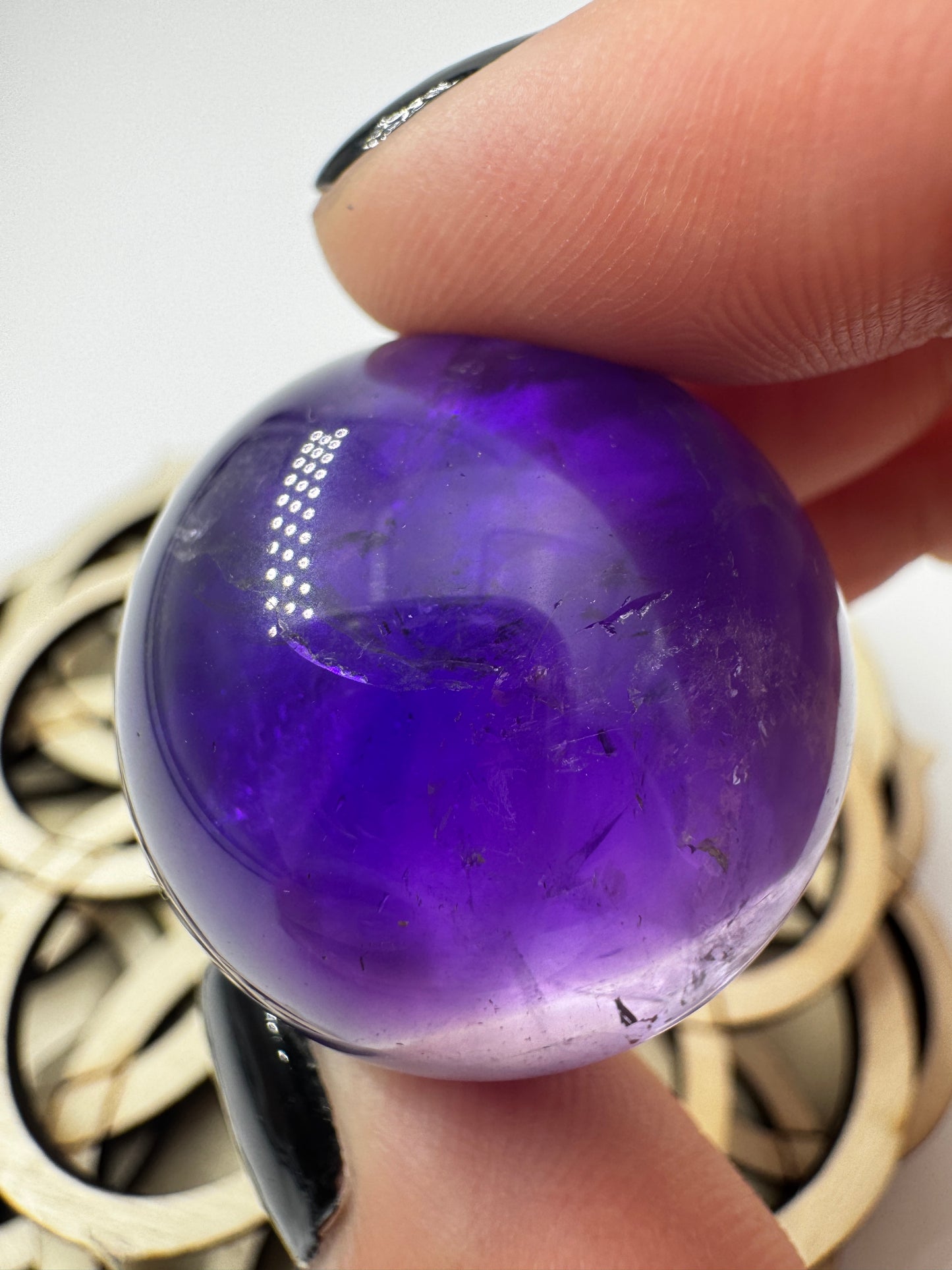 Eine hochglanzpolierte Amethyst-Kugel mit tiefvioletten Farbzentren und natürlichen Wachstumsstrukturen mit leichter Beleuchtung von hinten.