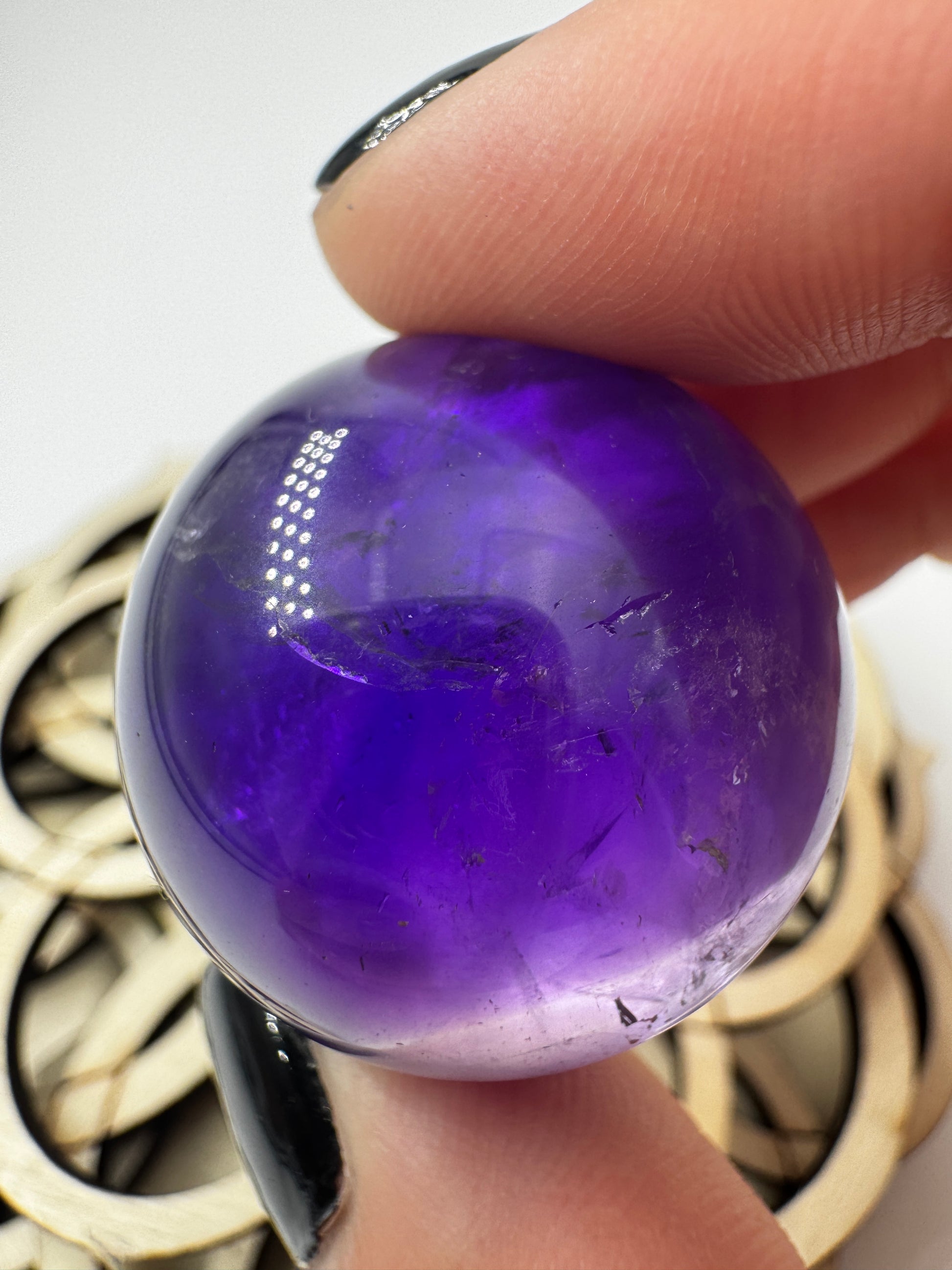 Eine hochglanzpolierte Amethyst-Kugel mit tiefvioletten Farbzentren und natürlichen Wachstumsstrukturen mit leichter Beleuchtung von hinten.