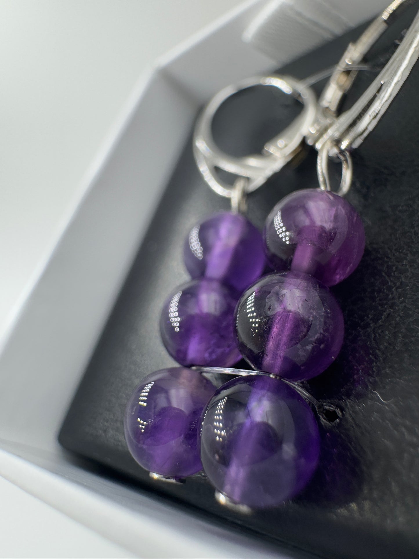 Ein Paar hochwertige Ohrhänger mit intensiv violetten Amethyst-Kugeln, deren transparente Struktur das Licht in feinen Facetten bricht.