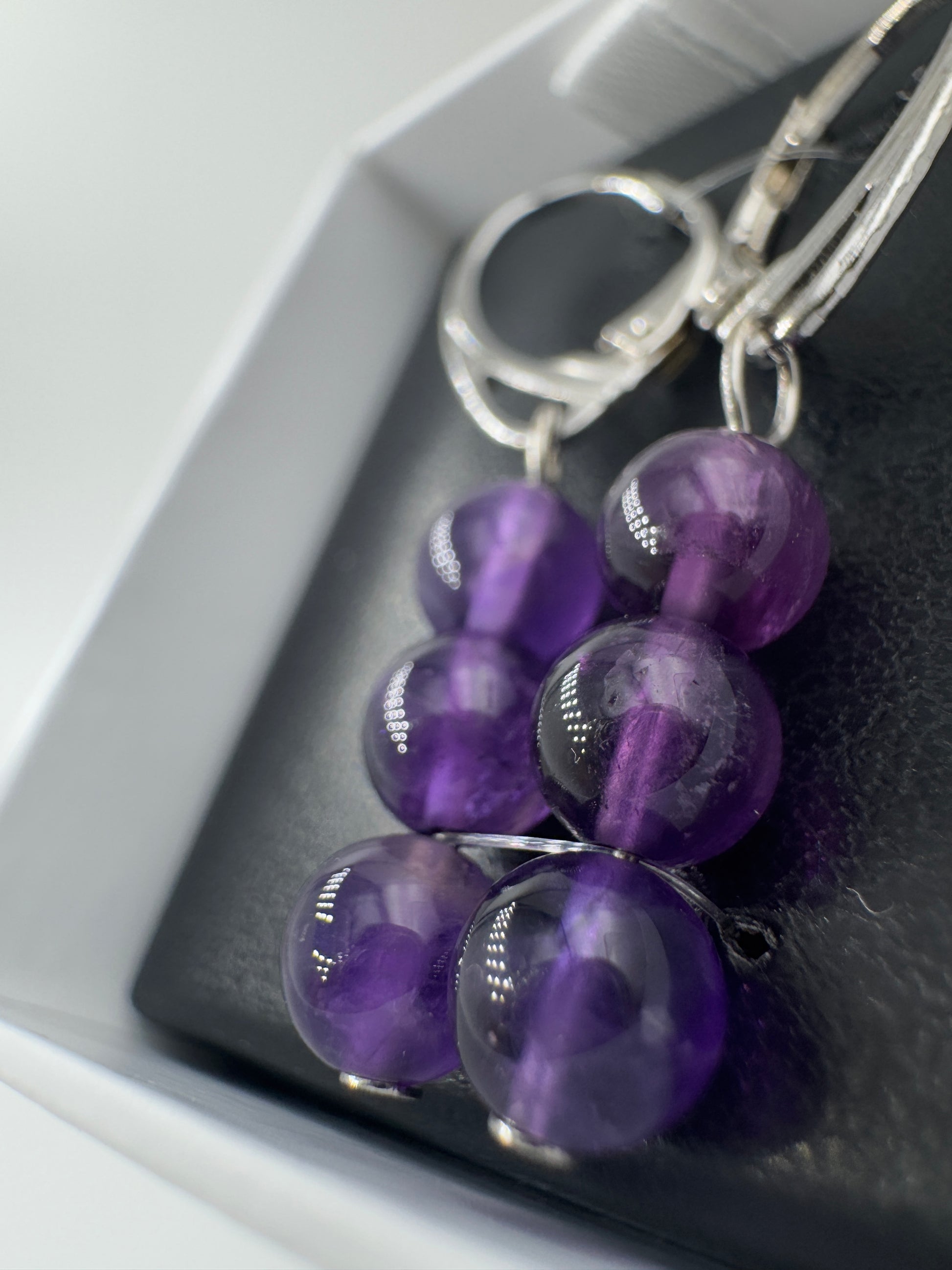 Ein Paar hochwertige Ohrhänger mit intensiv violetten Amethyst-Kugeln, deren transparente Struktur das Licht in feinen Facetten bricht.