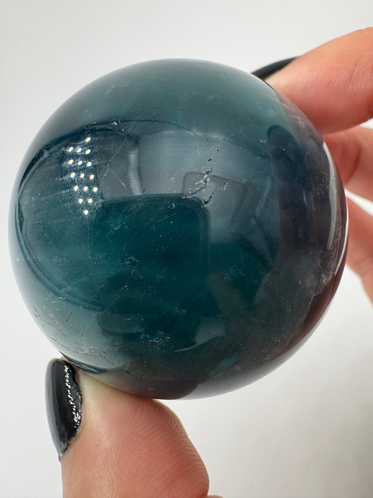 Eine tiefblaue, polierte Fluorit-Kugel mit inneren Wachstumsstrukturen und einem minimalen, authentischen Oberflächenmerkmal.