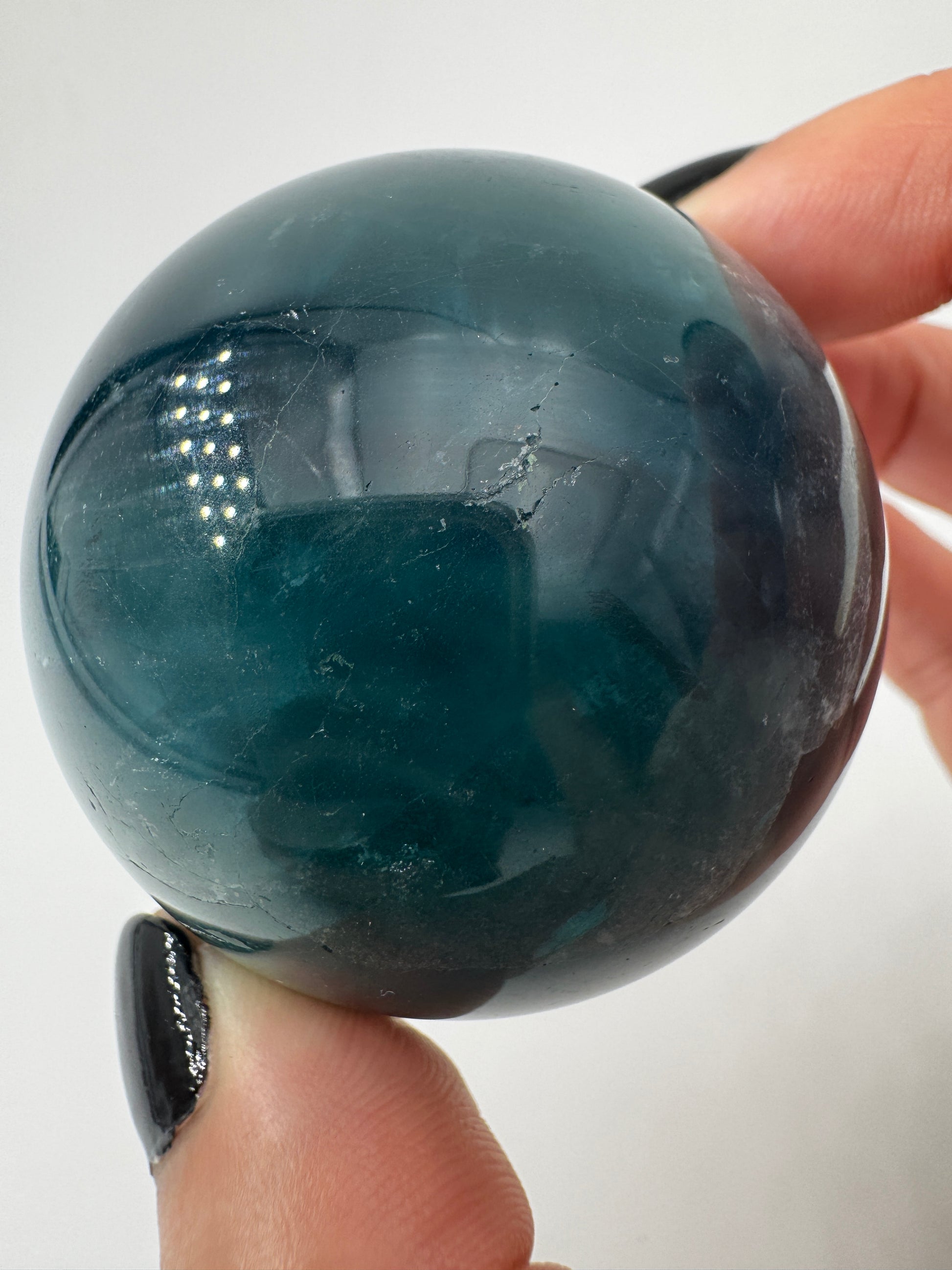 Eine tiefblaue, polierte Fluorit-Kugel mit inneren Wachstumsstrukturen und einem minimalen, authentischen Oberflächenmerkmal.