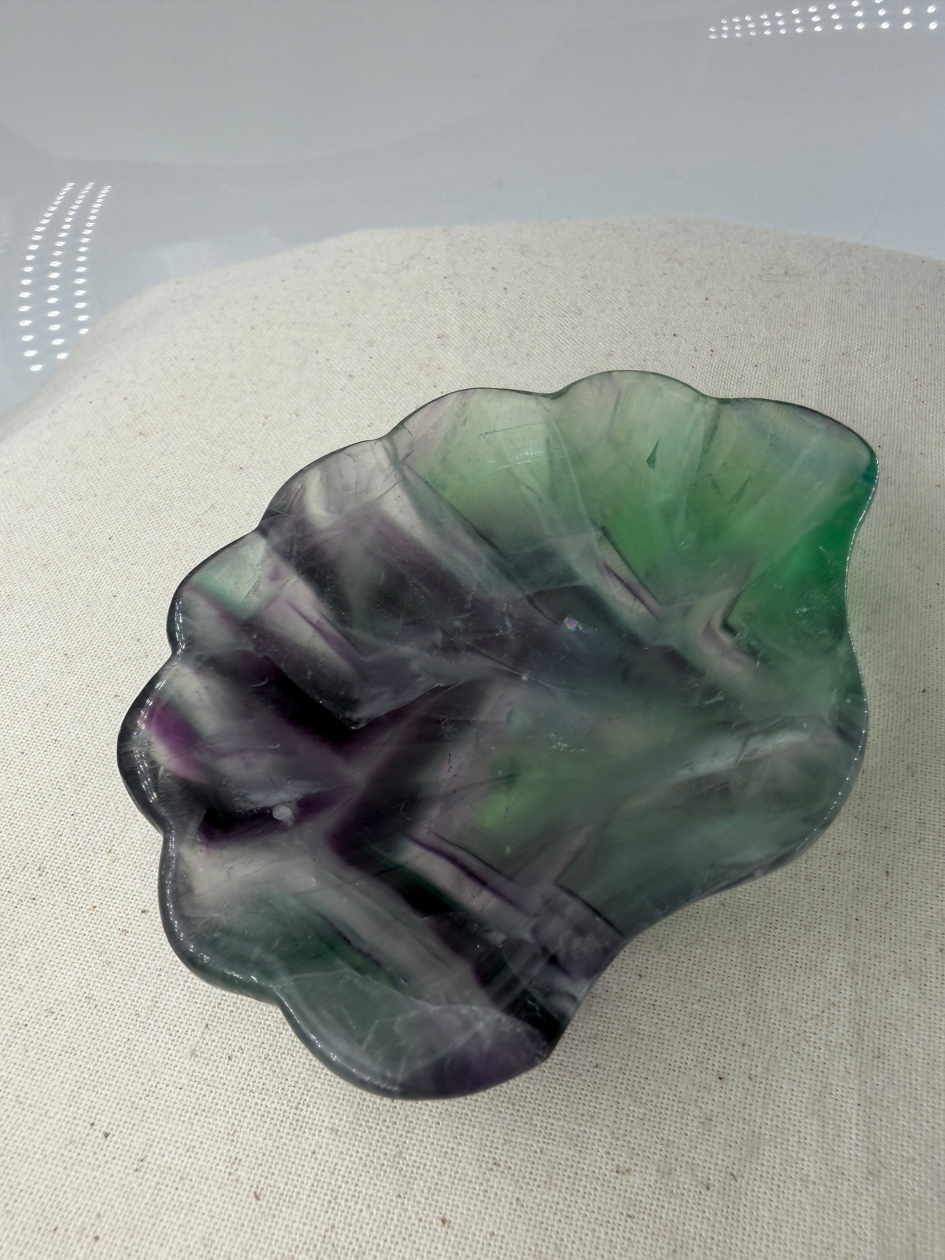 Eine kunstvoll geschnitzte Muschelschale aus transparentem Fluorit, die durch ihre natürlichen, violetten und grünen Farbbänderungen sowie eine seidig glänzende Politur besticht.