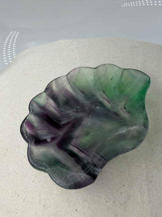 Eine kunstvoll geschnitzte Muschelschale aus transparentem Fluorit, die durch ihre natürlichen, violetten und grünen Farbbänderungen sowie eine seidig glänzende Politur besticht.