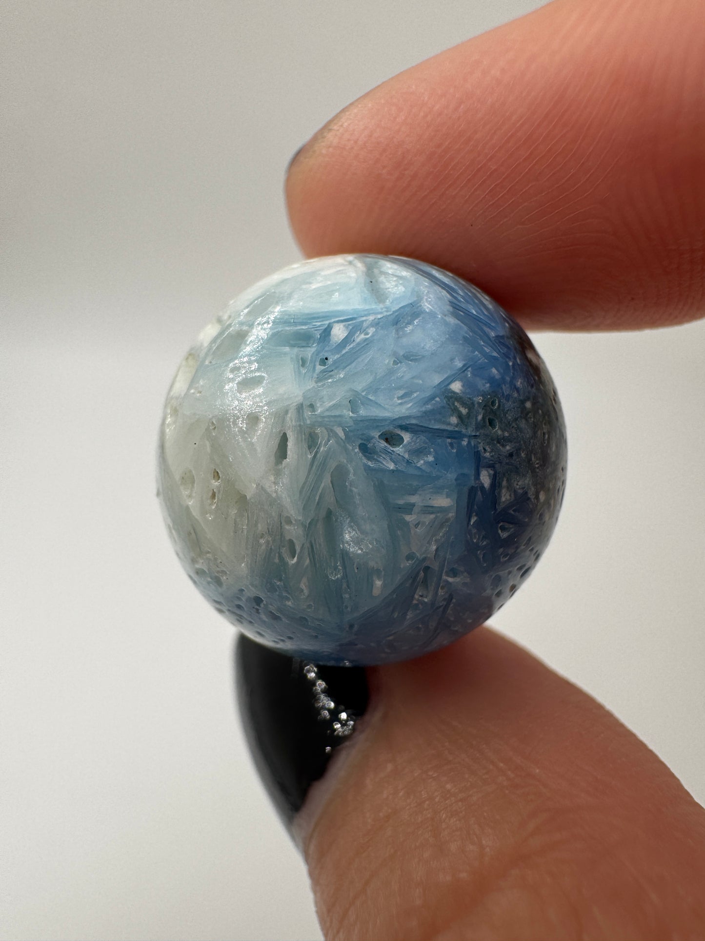 Eine perfekt sphärische Kugel aus Blue Ice Glacierite, deren glänzende Oberfläche das Licht reflektiert und den Blick auf die einmalige Strucktur freigibt.
