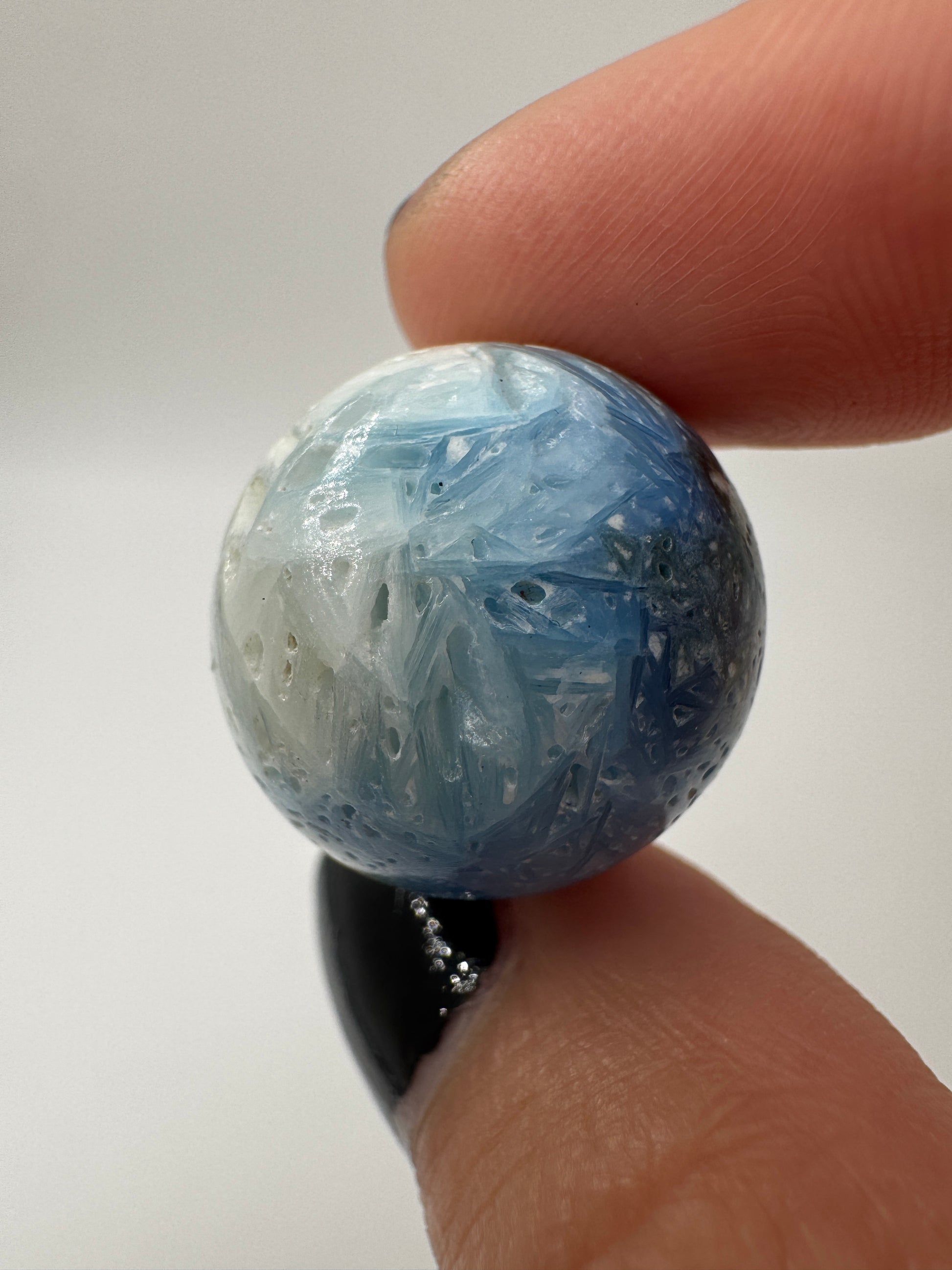 Eine perfekt sphärische Kugel aus Blue Ice Glacierite, deren glänzende Oberfläche das Licht reflektiert und den Blick auf die einmalige Strucktur freigibt.