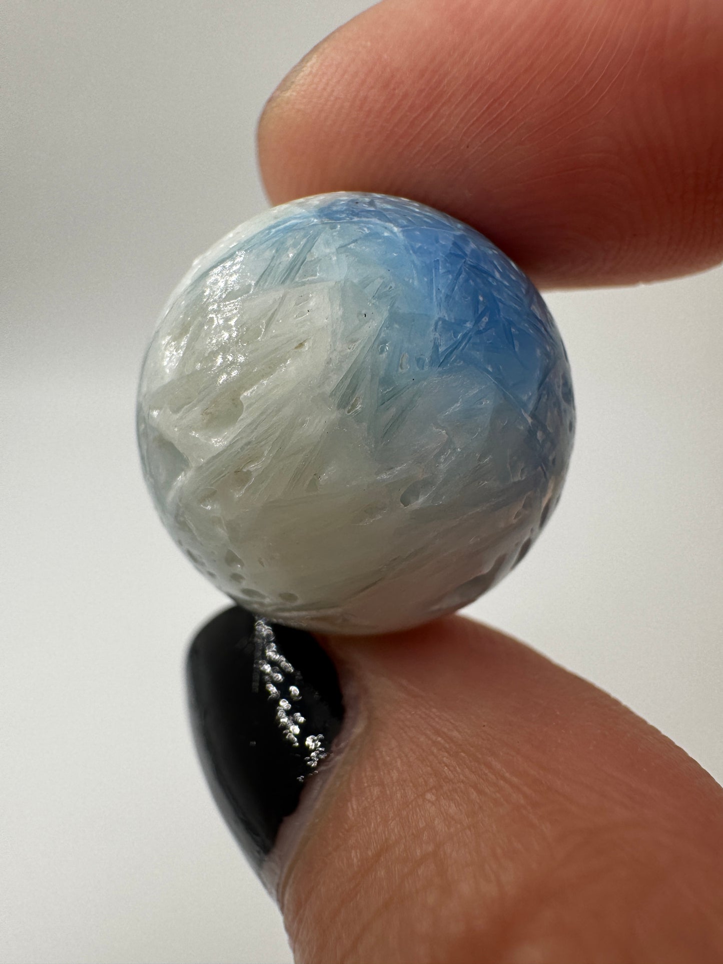 Eine perfekt sphärische Kugel aus Blue Ice Glacierite, deren glänzende Oberfläche das Licht reflektiert und den Blick auf die einmalige Strucktur freigibt.
