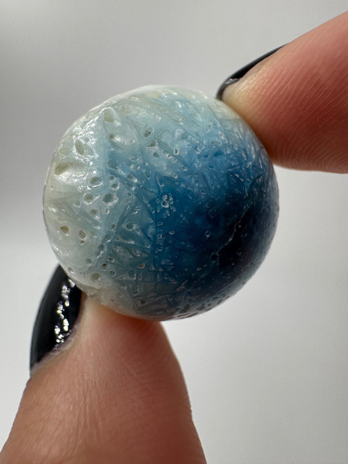 Eine perfekt sphärische Kugel aus Blue Ice Glacierite, deren glänzende Oberfläche das Licht reflektiert und den Blick auf die einmalige Strucktur freigibt.