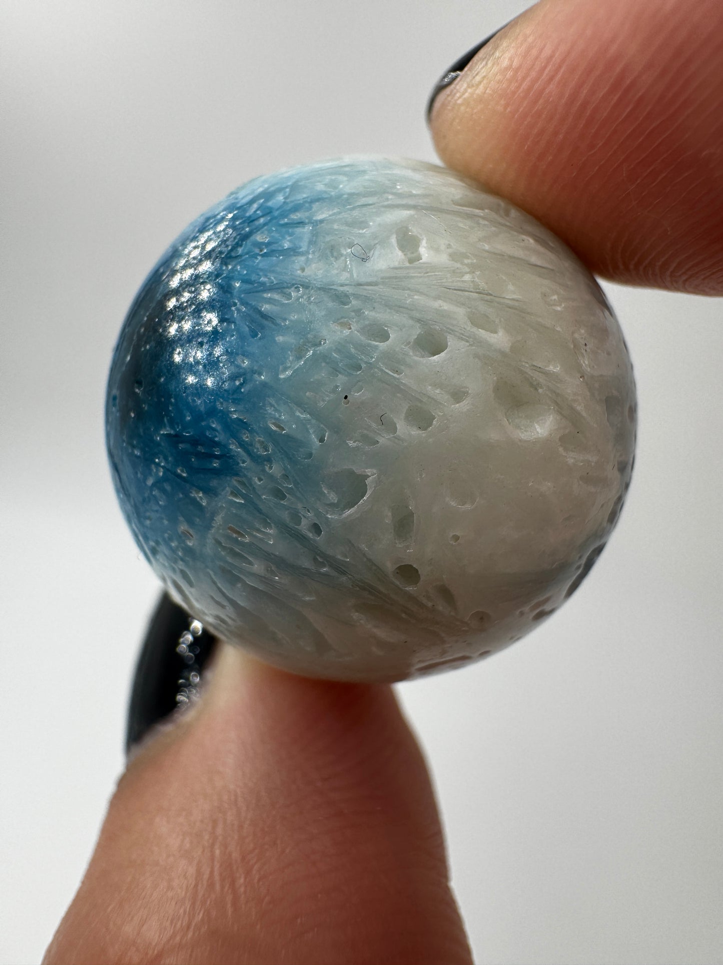 Eine perfekt sphärische Kugel aus Blue Ice Glacierite, deren glänzende Oberfläche das Licht reflektiert und den Blick auf die einmalige Struktur freigibt.