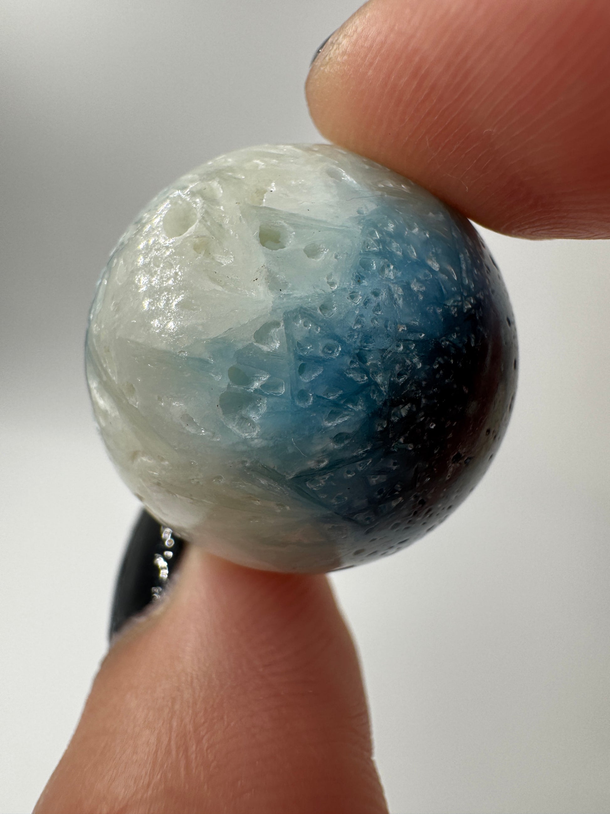 Eine perfekt sphärische Kugel aus Blue Ice Glacierite, deren glänzende Oberfläche das Licht reflektiert und den Blick auf die einmalige Struktur freigibt.