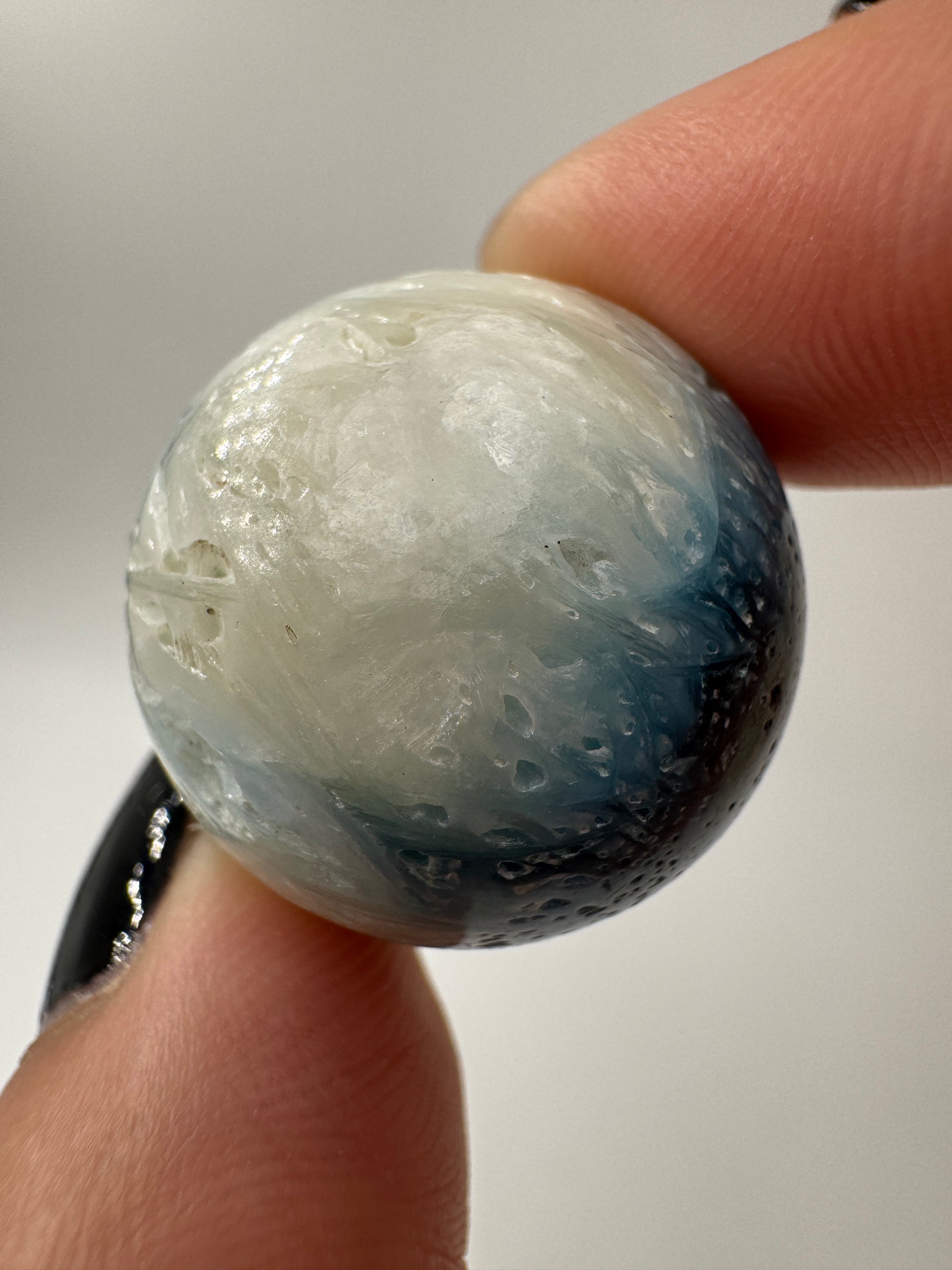 Eine perfekt sphärische Kugel aus Blue Ice Glacierite, deren glänzende Oberfläche das Licht reflektiert und den Blick auf die einmalige Struktur freigibt.