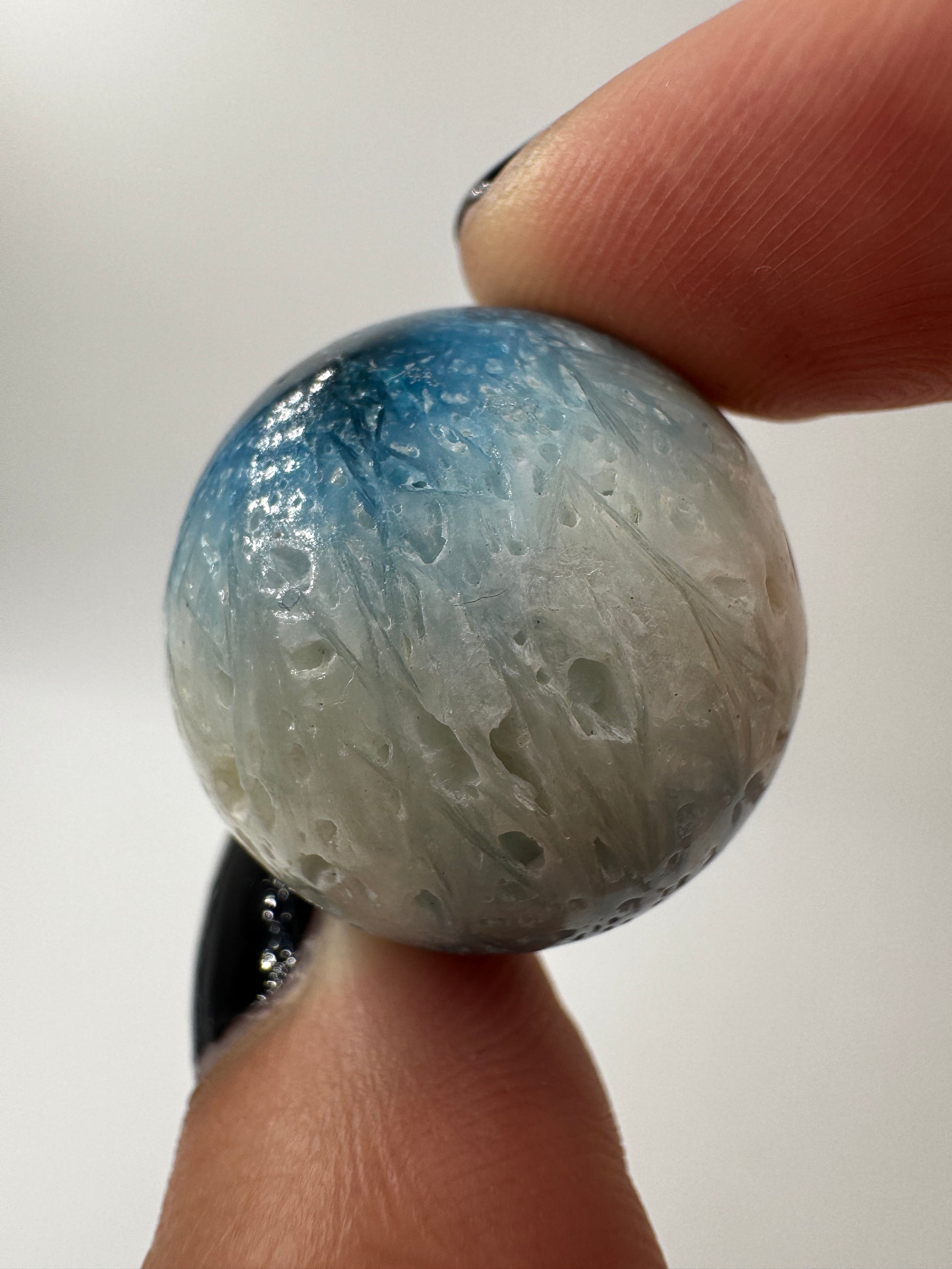 Eine perfekt sphärische Kugel aus Blue Ice Glacierite, deren glänzende Oberfläche das Licht reflektiert und den Blick auf die einmalige Struktur freigibt.