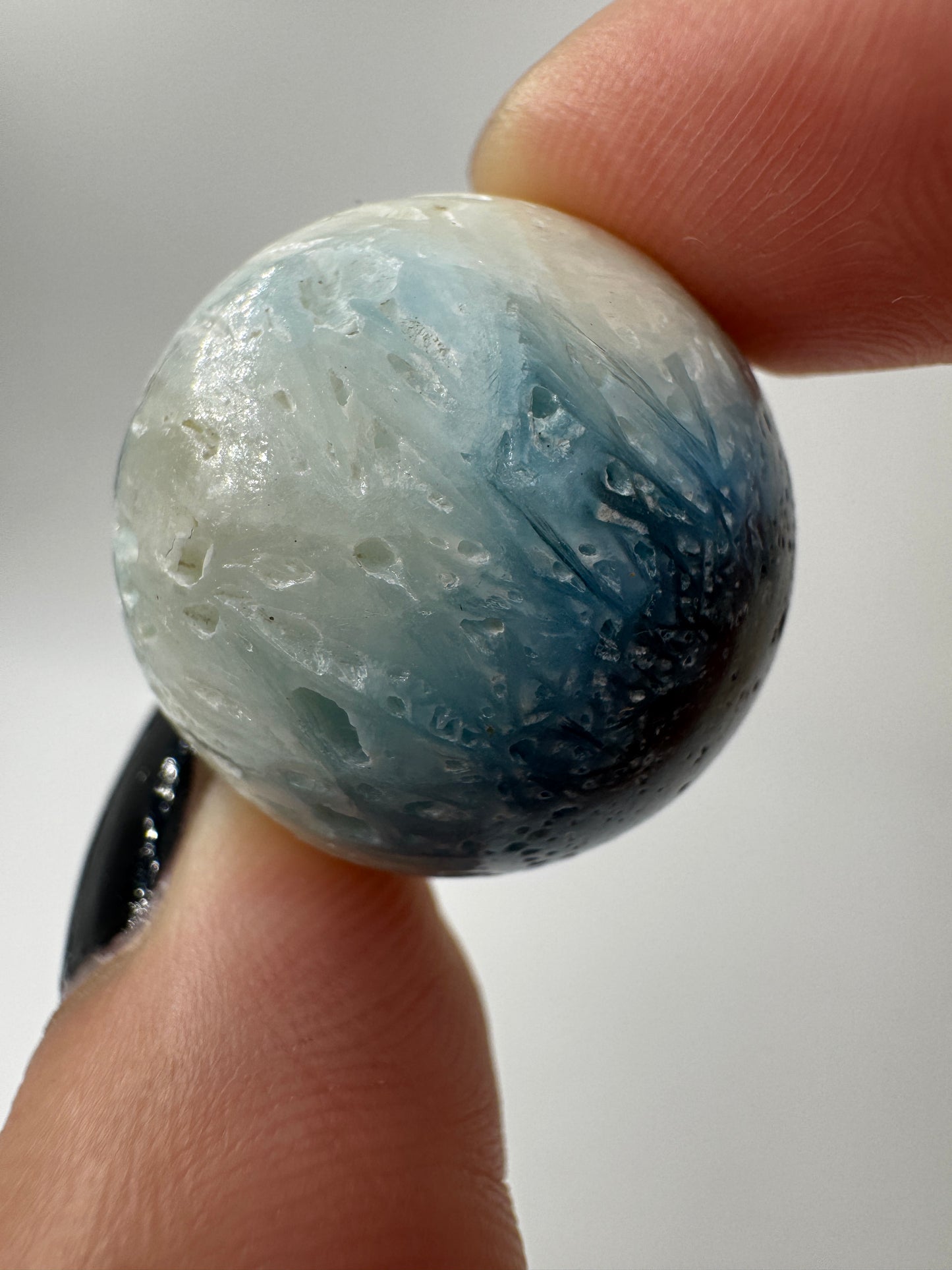 Eine perfekt sphärische Kugel aus Blue Ice Glacierite, deren glänzende Oberfläche das Licht reflektiert und den Blick auf die einmalige Struktur freigibt.