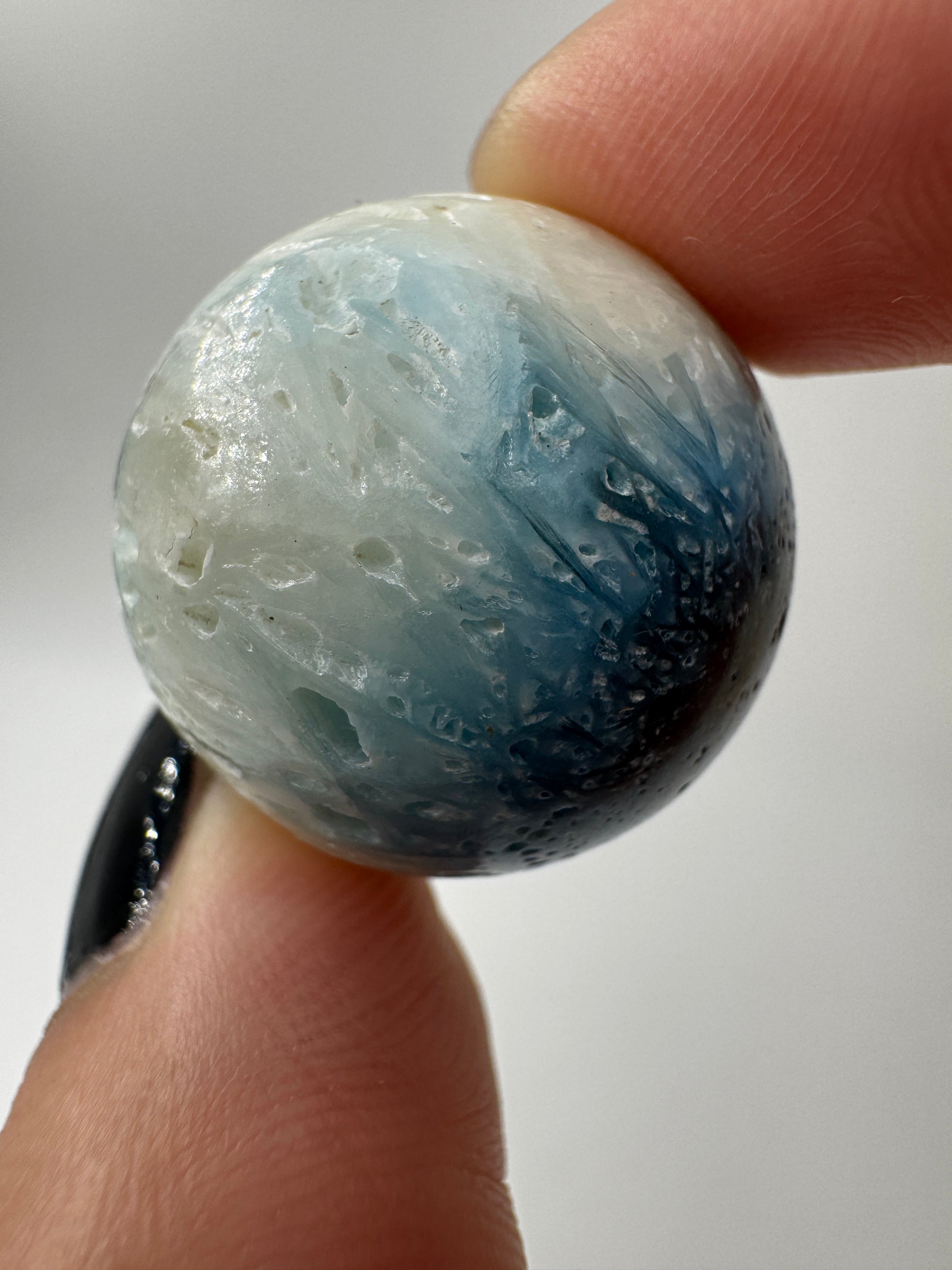 Eine perfekt sphärische Kugel aus Blue Ice Glacierite, deren glänzende Oberfläche das Licht reflektiert und den Blick auf die einmalige Struktur freigibt.