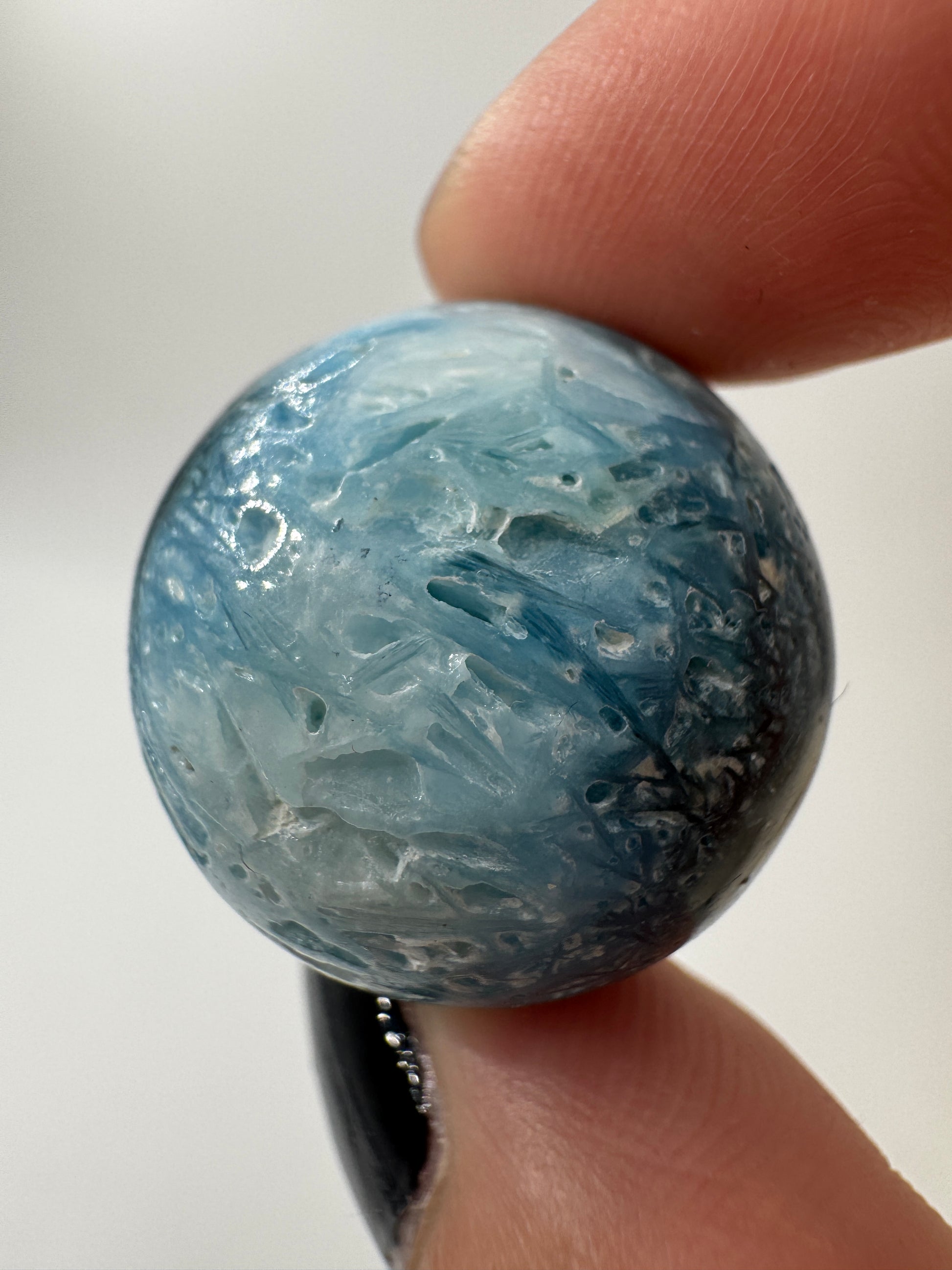 Eine perfekt sphärische Kugel aus Blue Ice Glacierite, deren glänzende Oberfläche das Licht reflektiert und den Blick auf die einmalige Struktur freigibt.