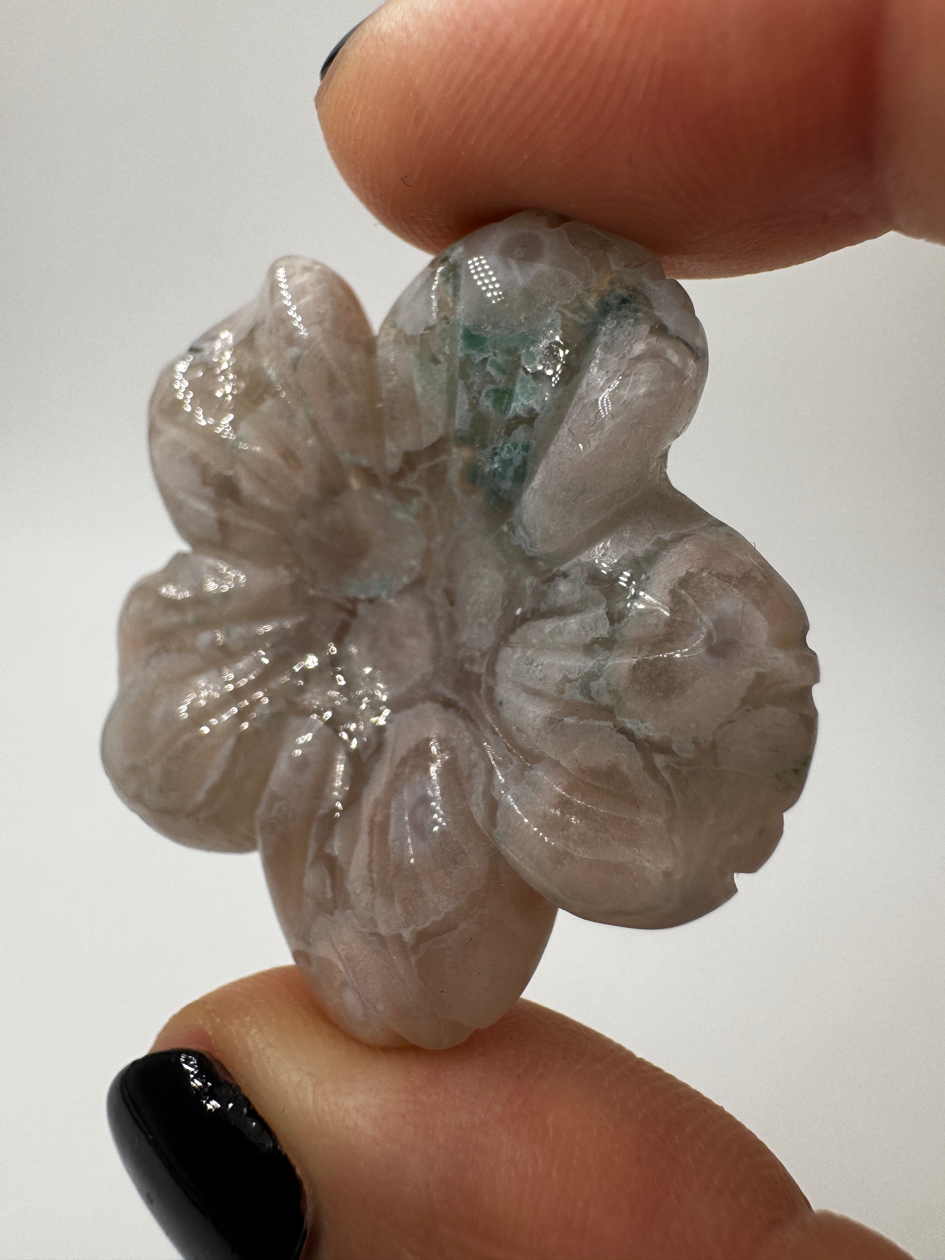 Eine detailreiche Skulptur in Blumenform aus zartrosa Blumenachat mit deutlich erkennbaren, weißen sphärolithischen Einschlüssen.
