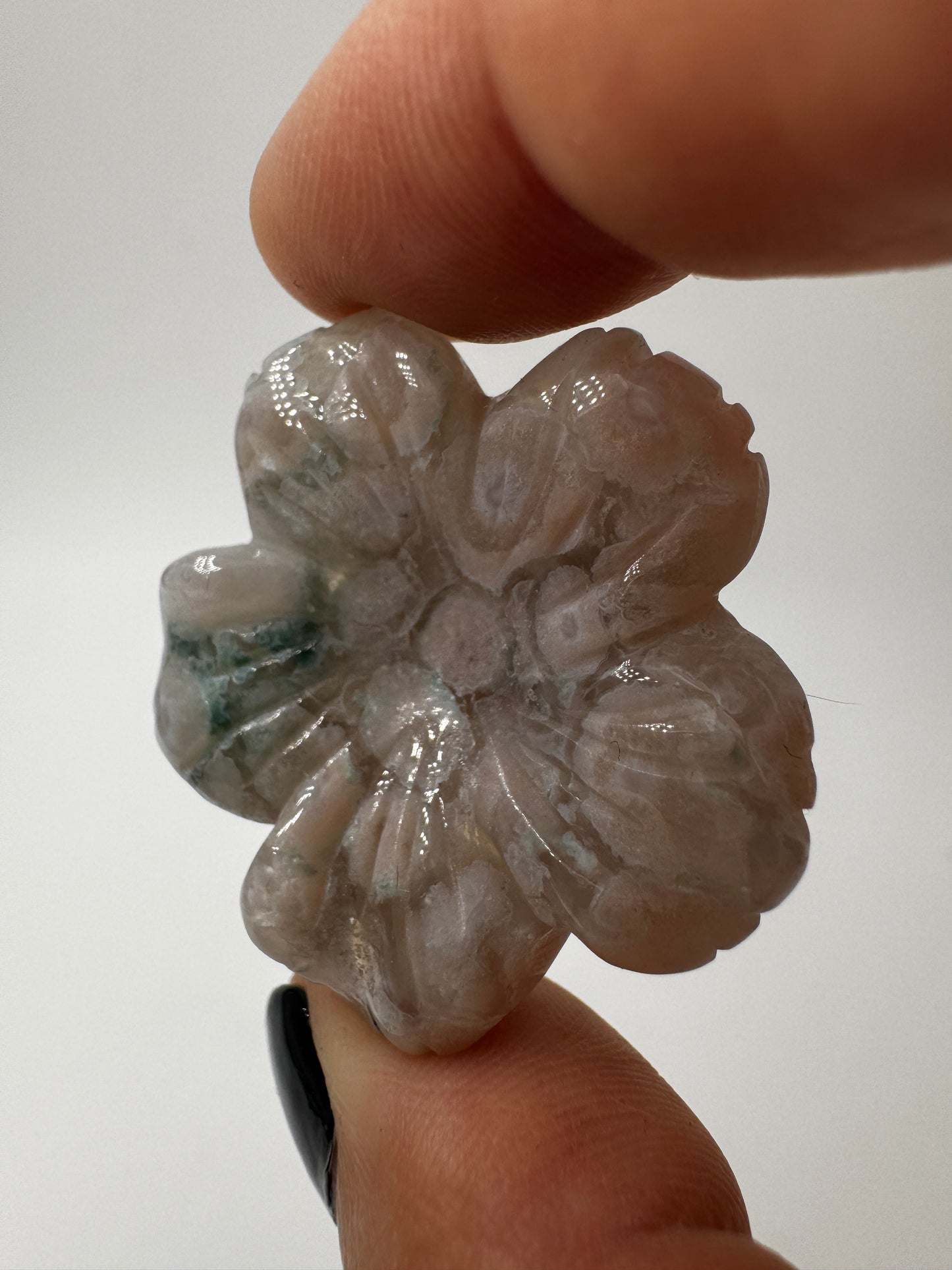 Eine detailreiche Skulptur in Blumenform aus zartrosa Blumenachat mit deutlich erkennbaren, weißen sphärolithischen Einschlüssen.