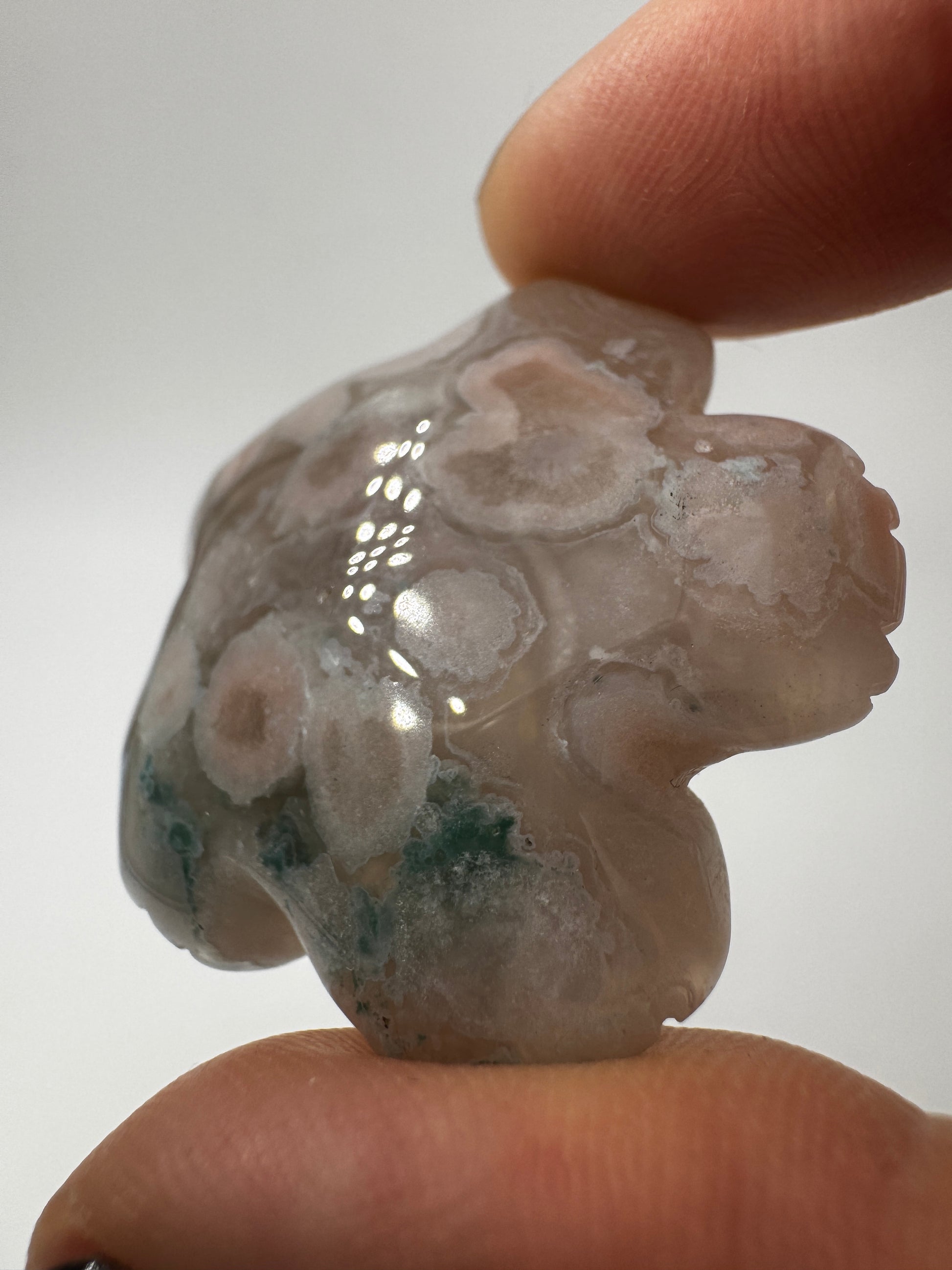 Eine detailreiche Skulptur in Blumenform aus zartrosa Blumenachat mit deutlich erkennbaren, weißen sphärolithischen Einschlüssen.