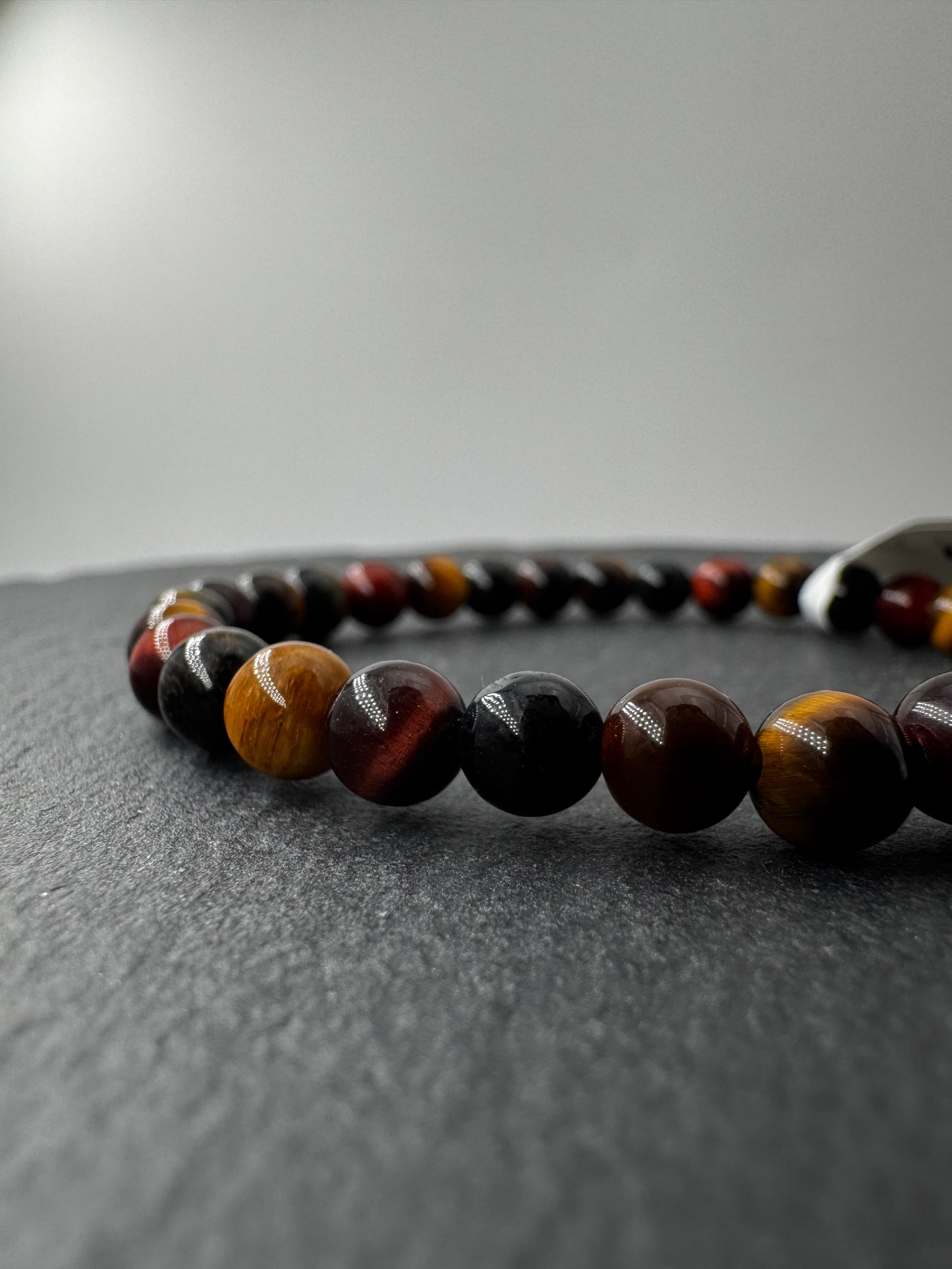 Nahaufnahme eines Kugelarmbands aus buntem Tigerauge in Blau-, Rot- und Goldtönen.