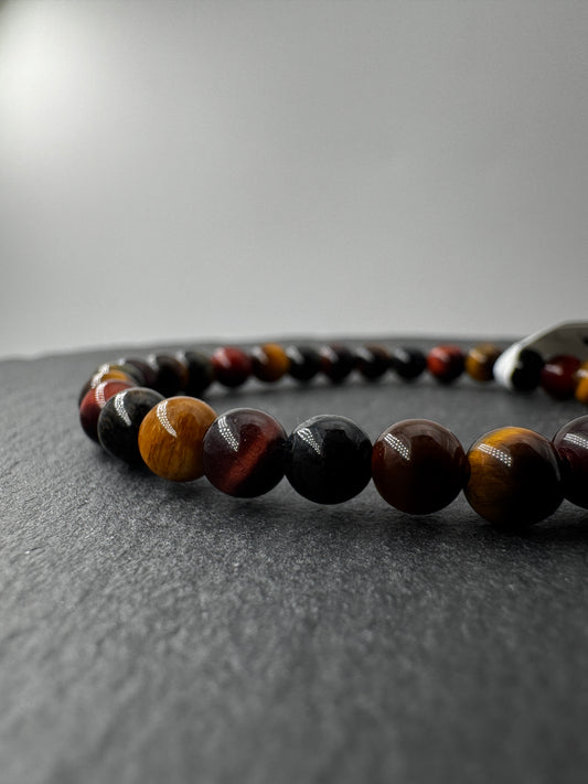 Nahaufnahme eines Kugelarmbands aus buntem Tigerauge in Blau-, Rot- und Goldtönen.