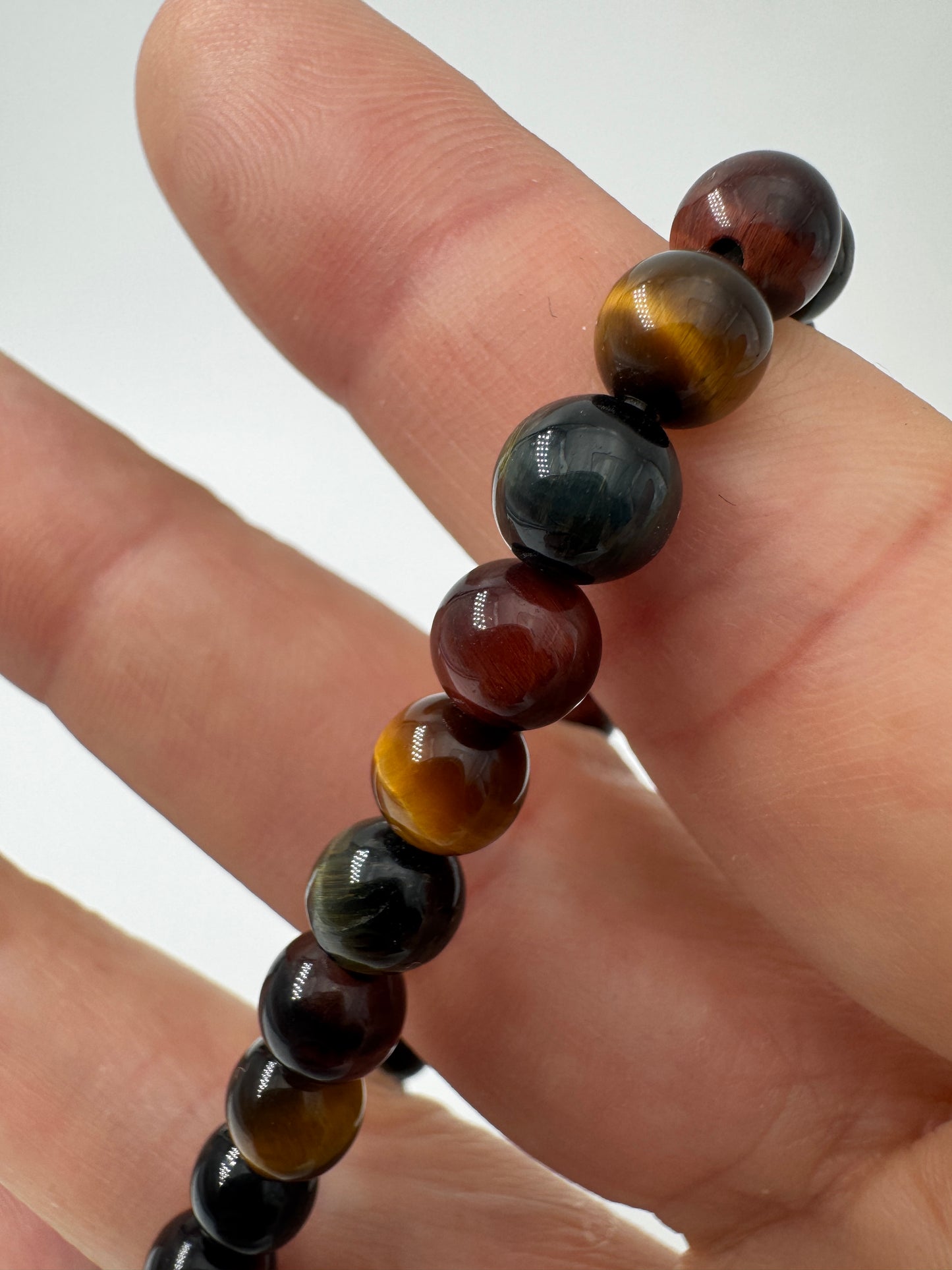 Nahaufnahme eines Kugelarmbands aus buntem Tigerauge in Blau-, Rot- und Goldtönen.
