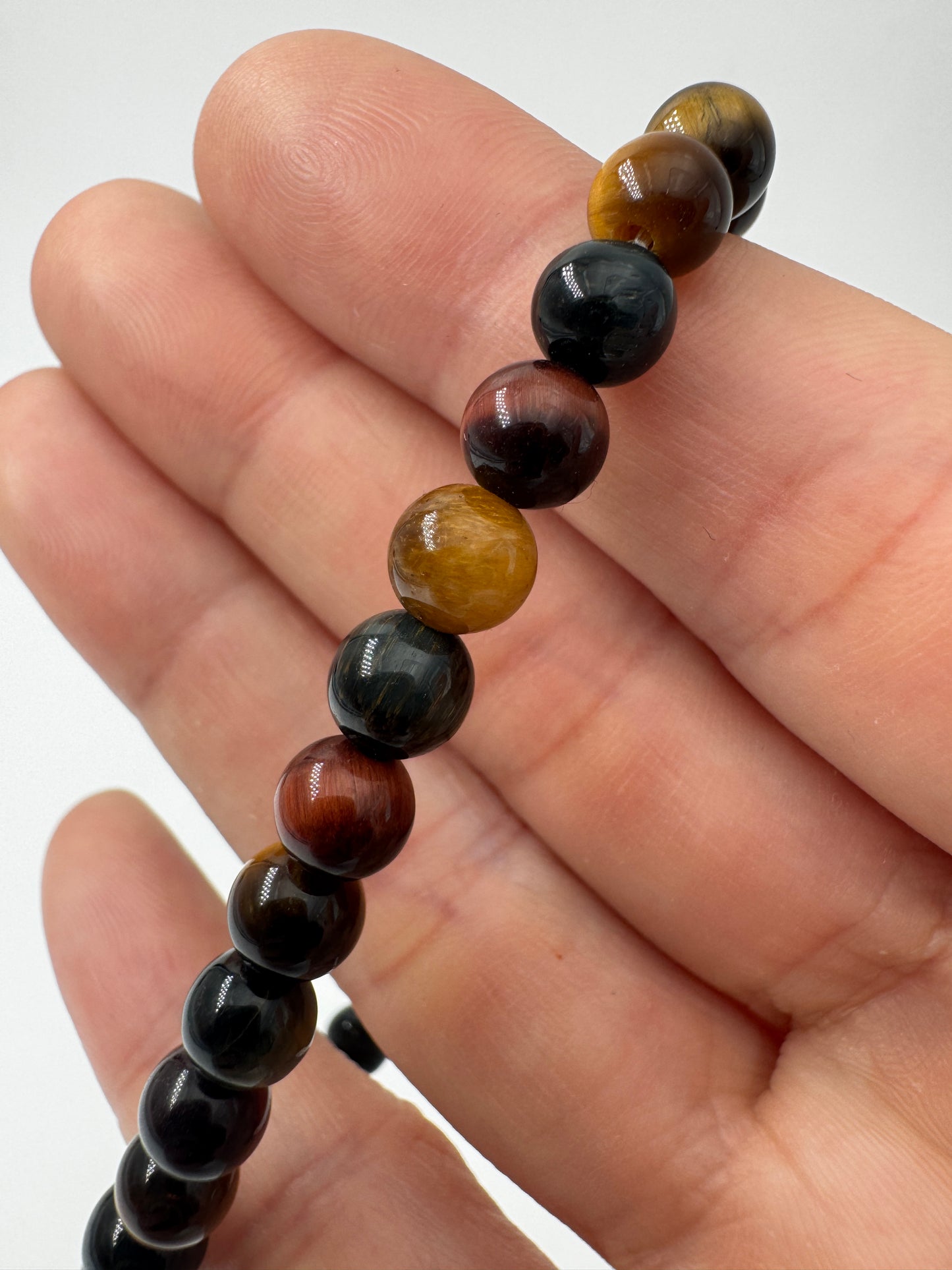 Nahaufnahme eines Kugelarmbands aus buntem Tigerauge in Blau-, Rot- und Goldtönen.