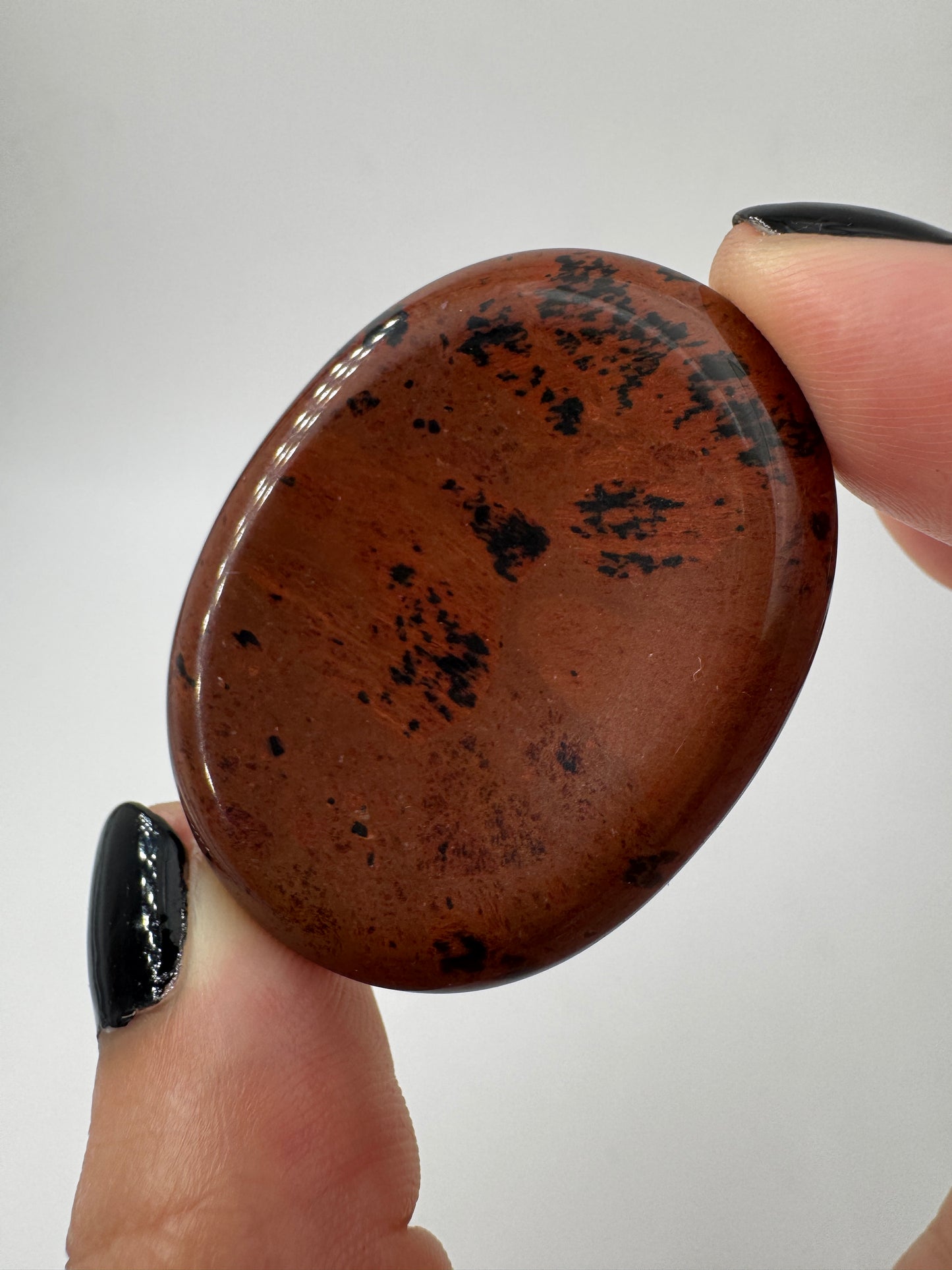 Ein  Daumensteinen aus Mahagoni Obsidian mit glänzend polierten Oberflächen und zentraler Daumenmulde.