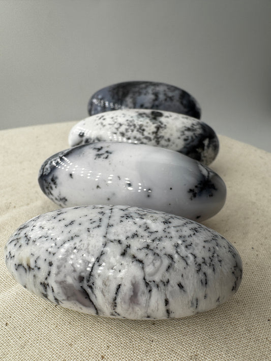 Ein eiförmig geschliffener, weißer Dendritenopal mit markanten, schwarzen Verästelungen und hochglänzender Oberfläche.