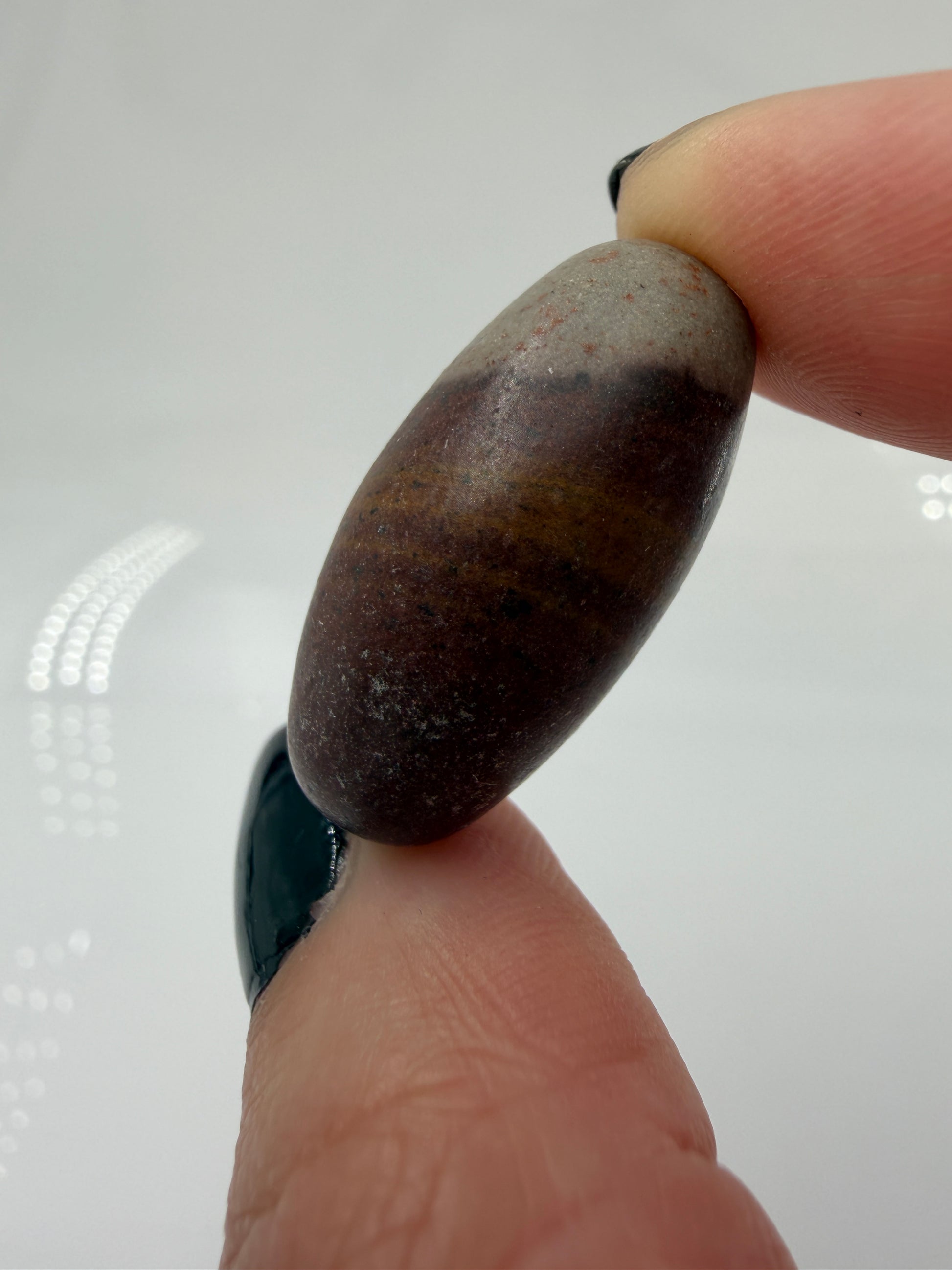 Kleiner, elliptisch geformter Shiva Lingam aus Indien mit markanter braun-roter Bänderung und glatter Oberfläche.