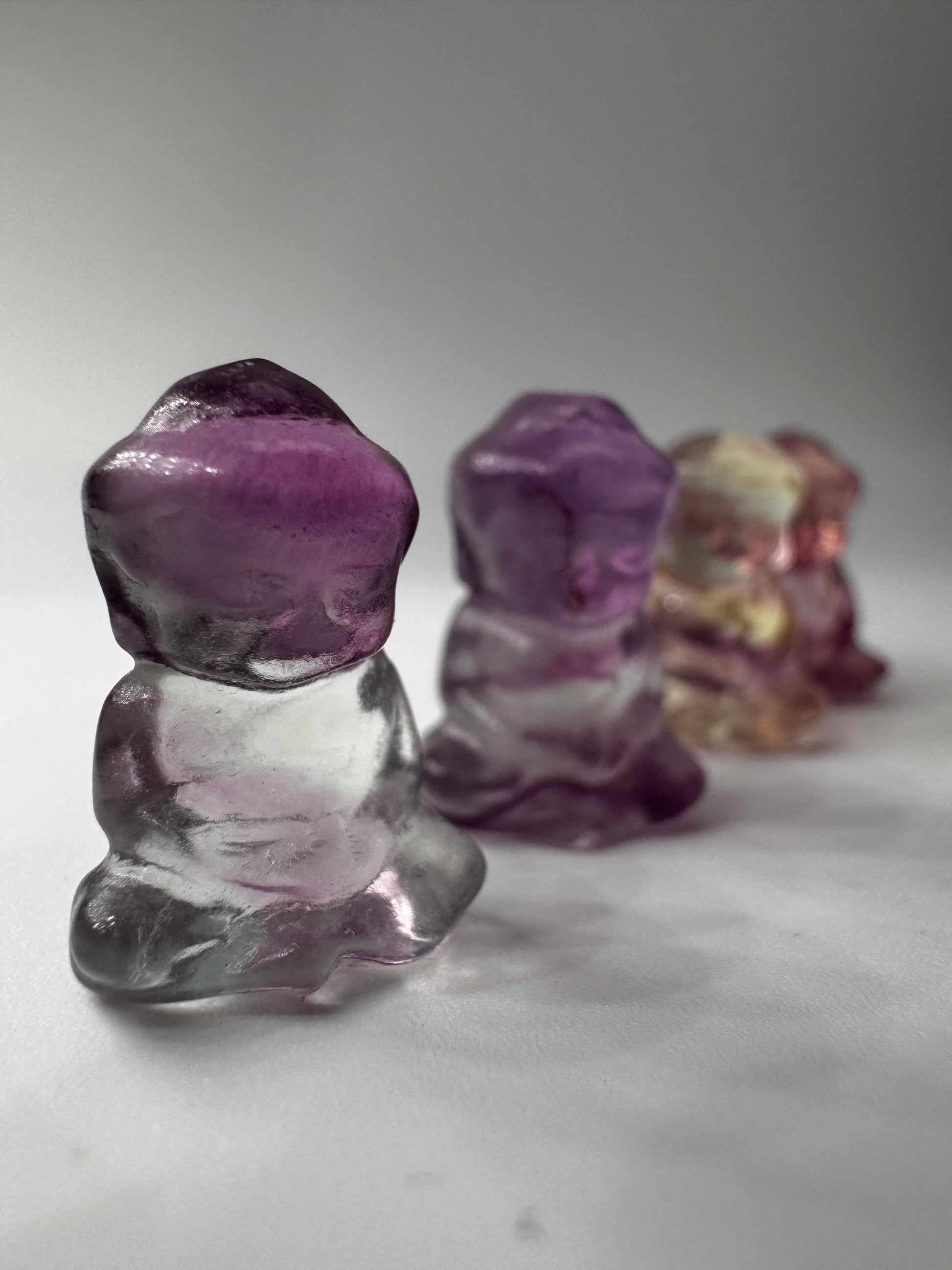 Miniatur-Buddha aus Fluorit FB3 mit glasartigem Glanz, erhältlich in Rosa, Lila, Lila-Blau und Gelb-Lila.