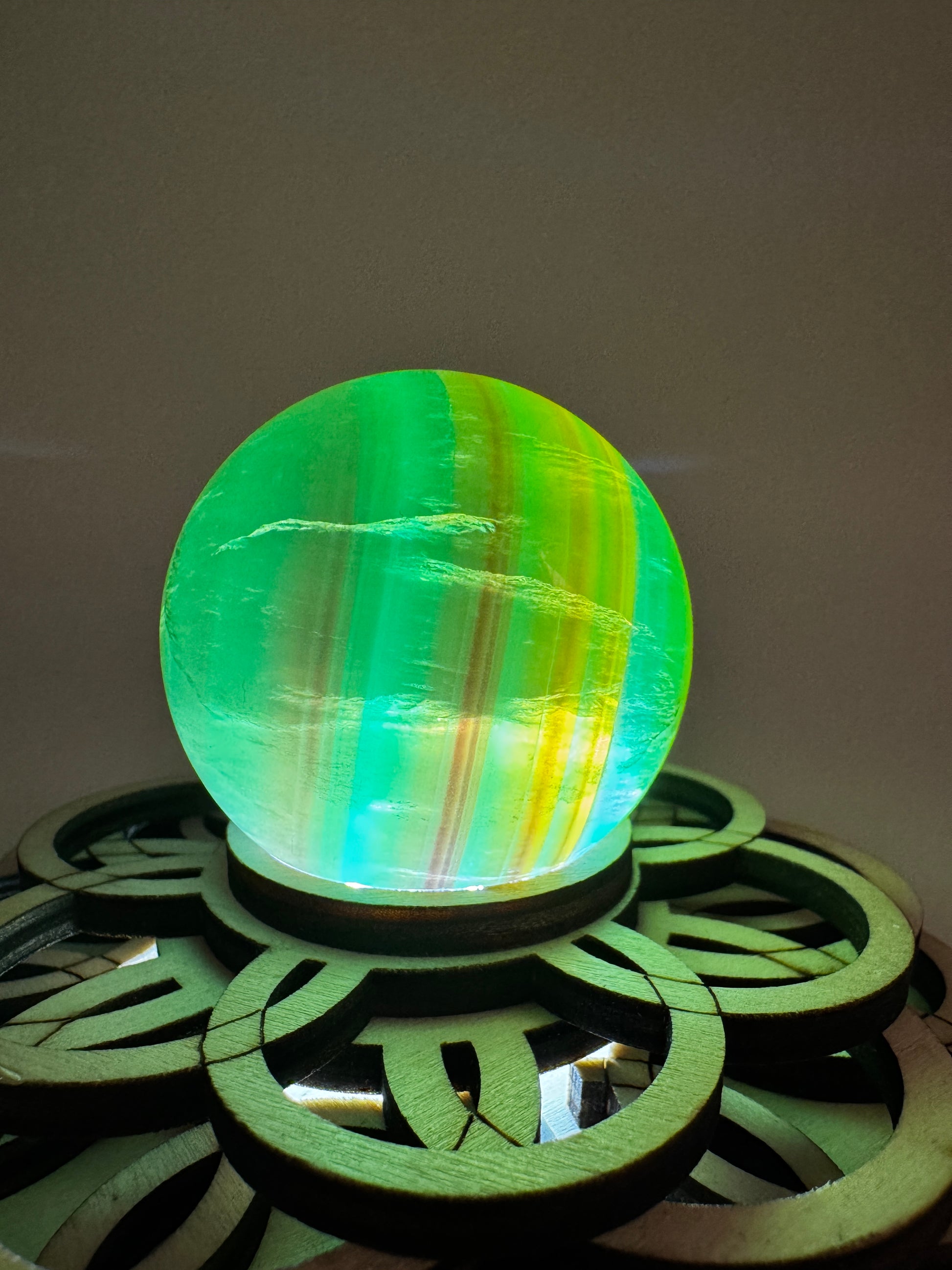 Eine Fluorit Kugel in Grün mit Bänderung auf einem Leuchtsockel.