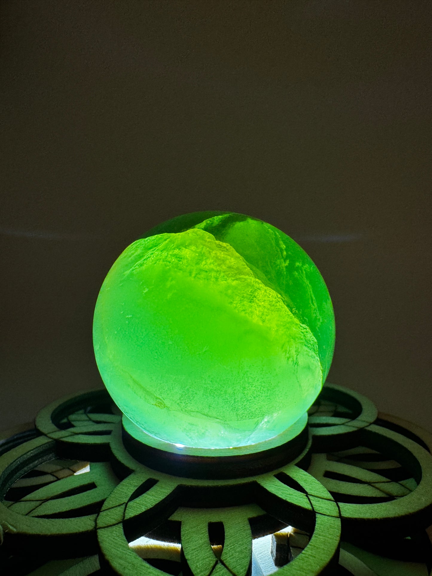 Eine Fluorit Kugel in Grün mit Bänderung auf einem Leuchtsockel.